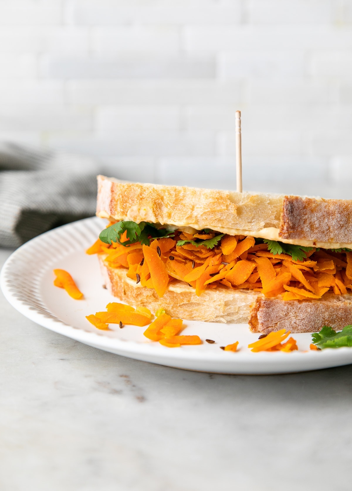 side angle view of carrot and hummus sandwich on a white plate.