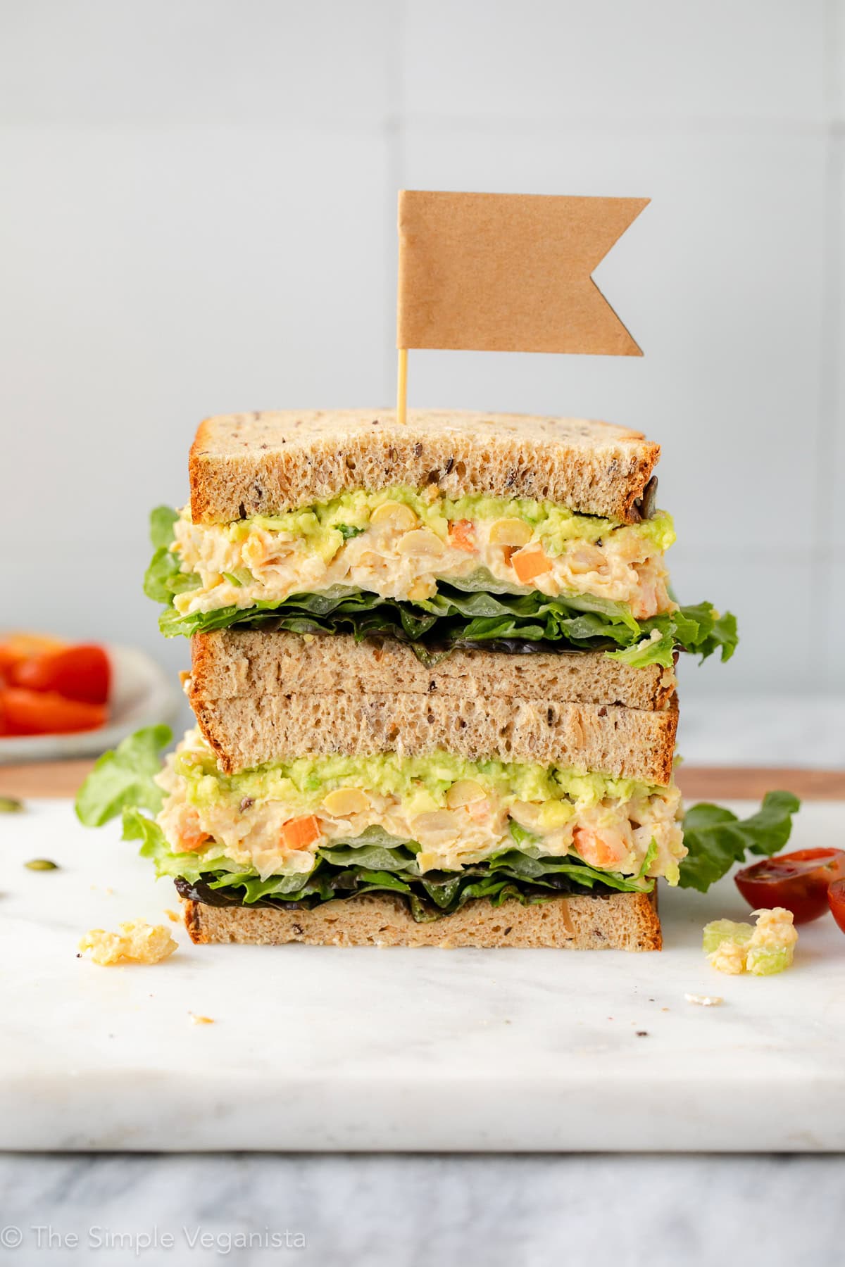 head on view of stacked halves of mashed chickpea salad sandwich on a marble slab with items surrounding.