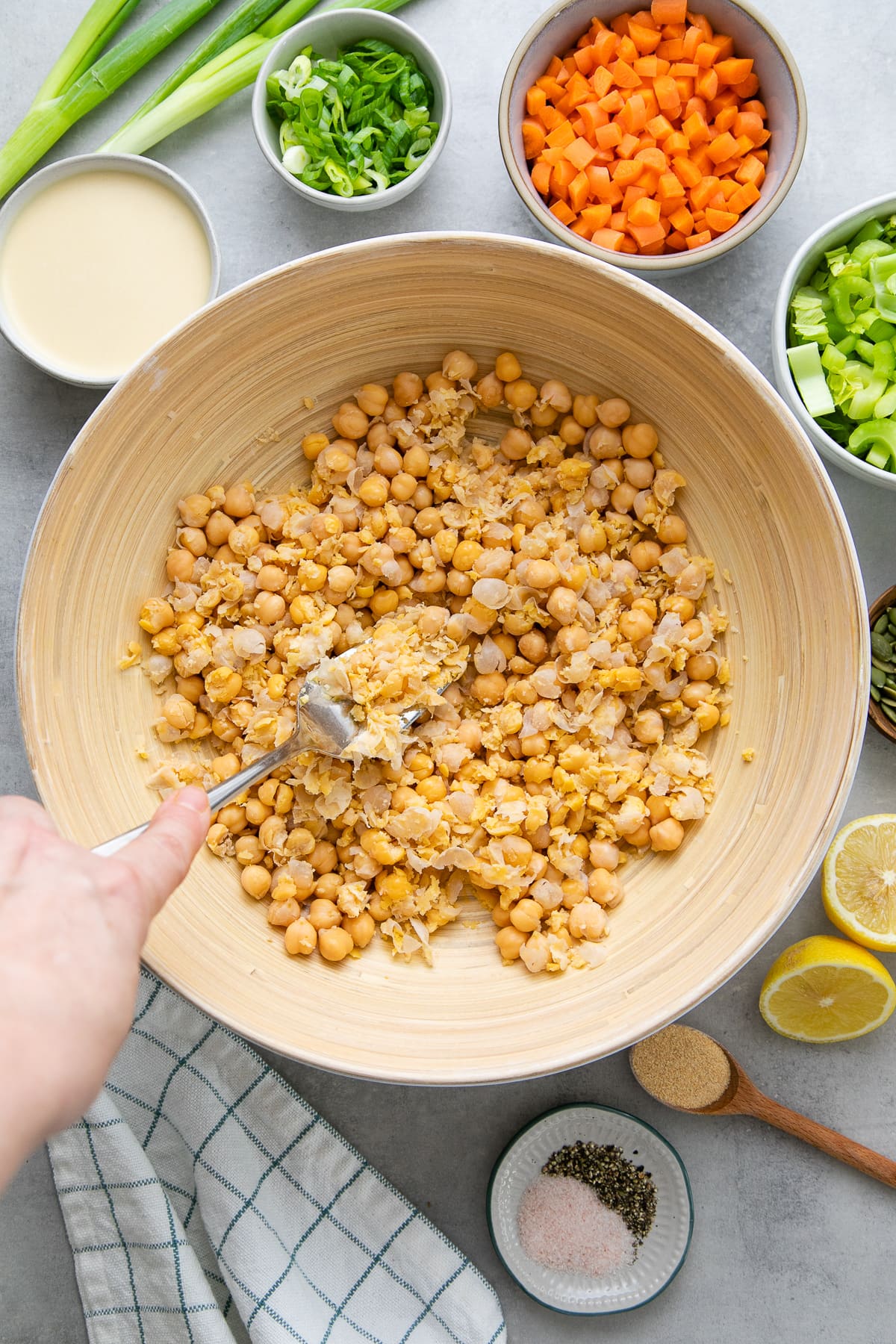 top down view showing the process of mashing chickpeas in a bowl with items surrounding.