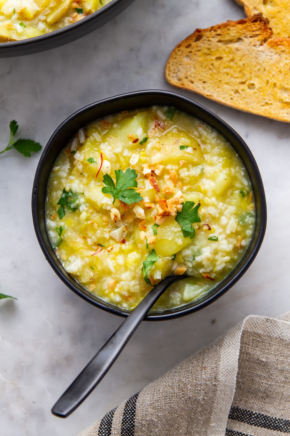 top down view of saffron potato leek soup in a bowl with spoon and items surrounded by items.