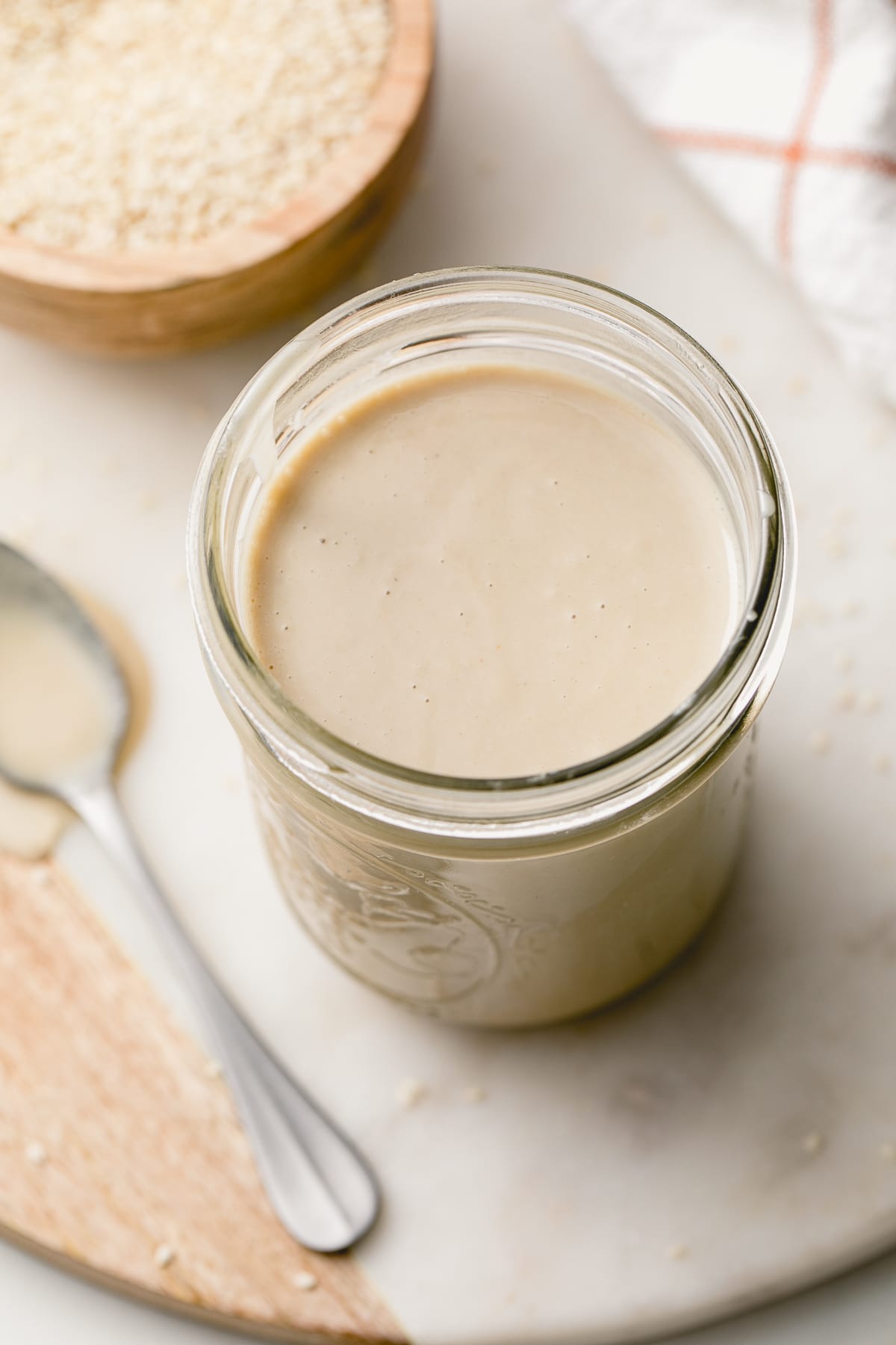 side angle view of easy homemade tahini in a jar with items surrounding.