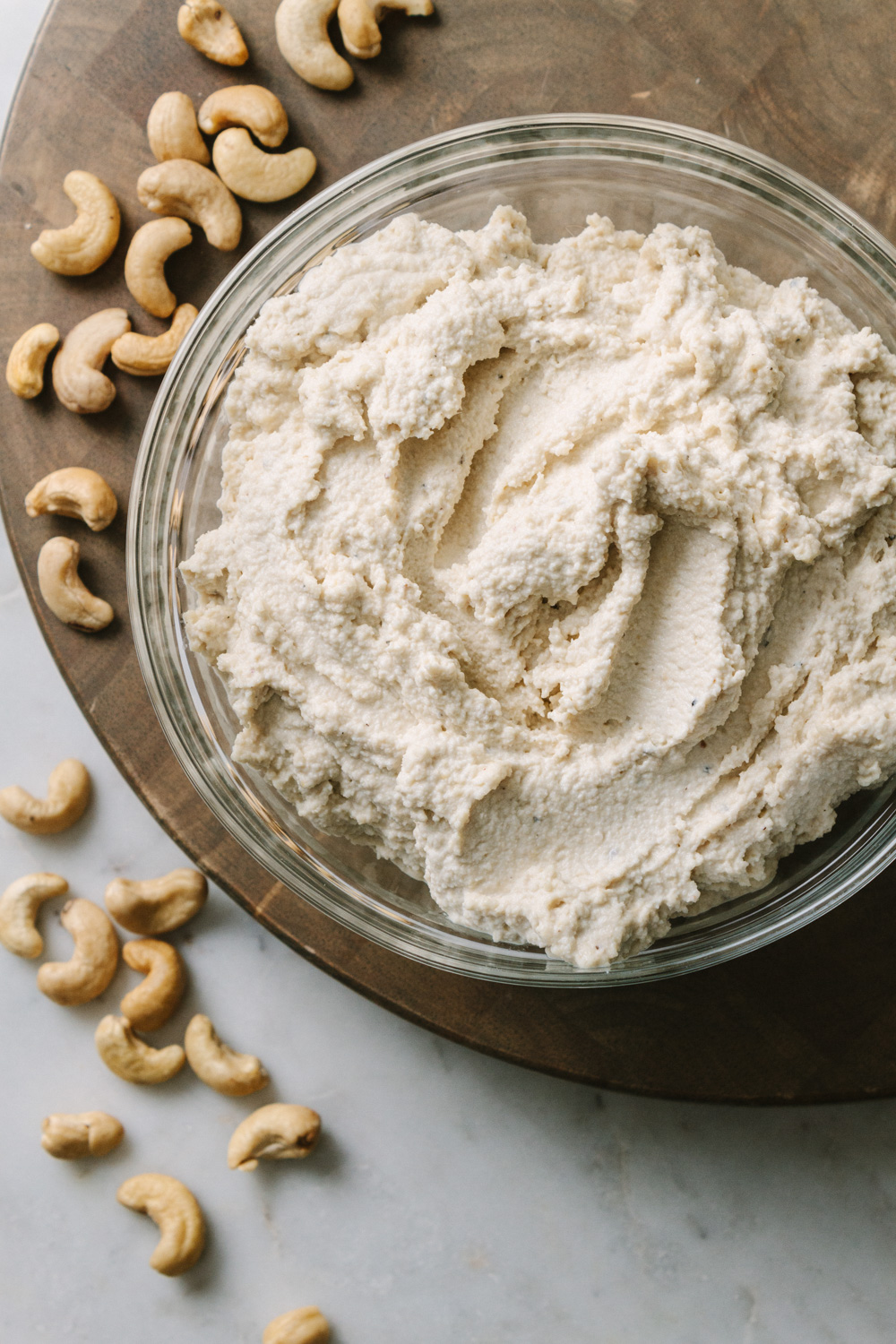 top down, close up view, of vegan cashew ricotta cheese in a glass bowl on a round wooden cutting board