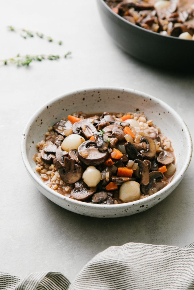 side angle view of handmade bowl with a serving of mushroom bourguignon and farro with items surrounding.