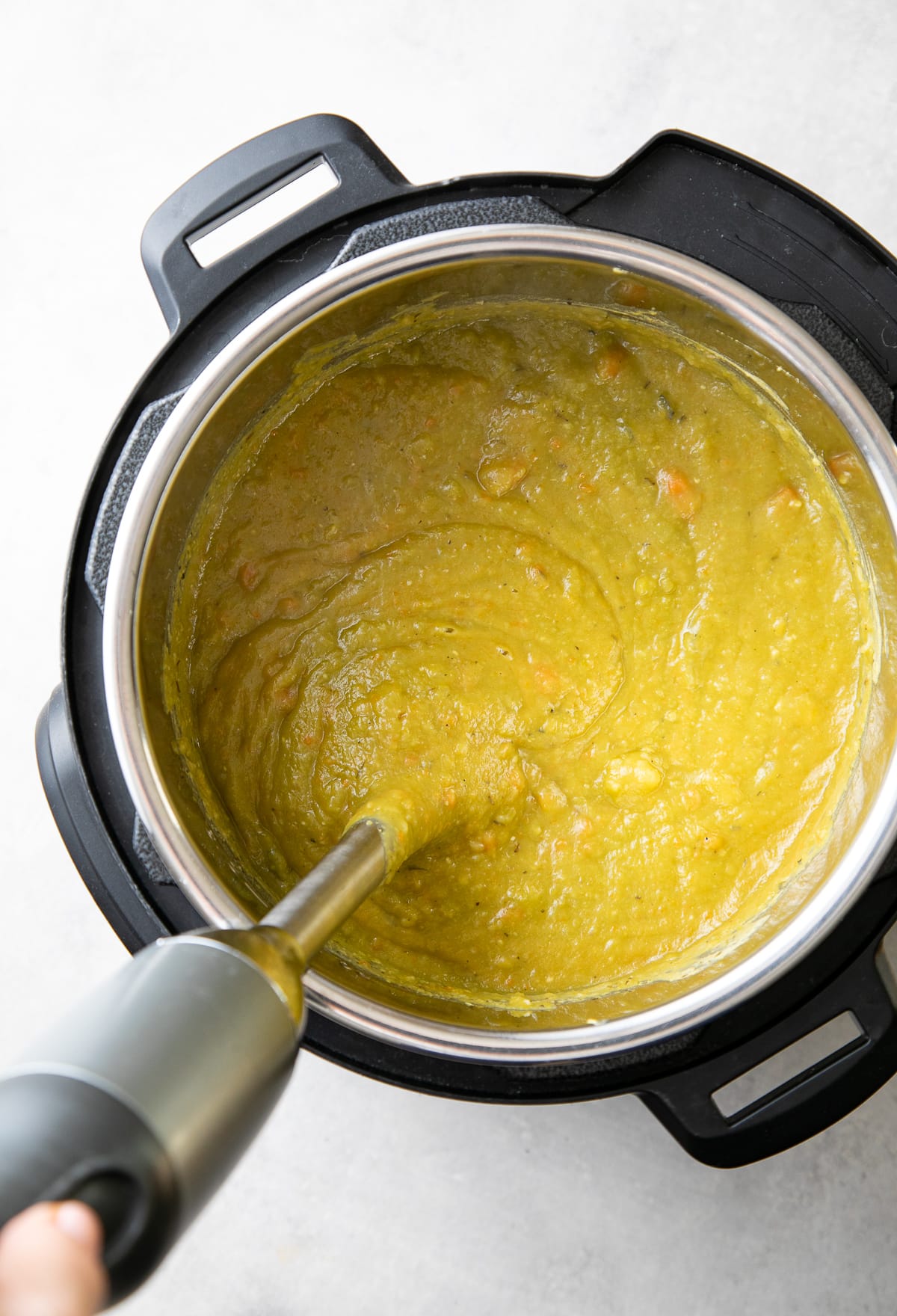 top down view showing the process of pureeing split pea soup with immersion blender.
