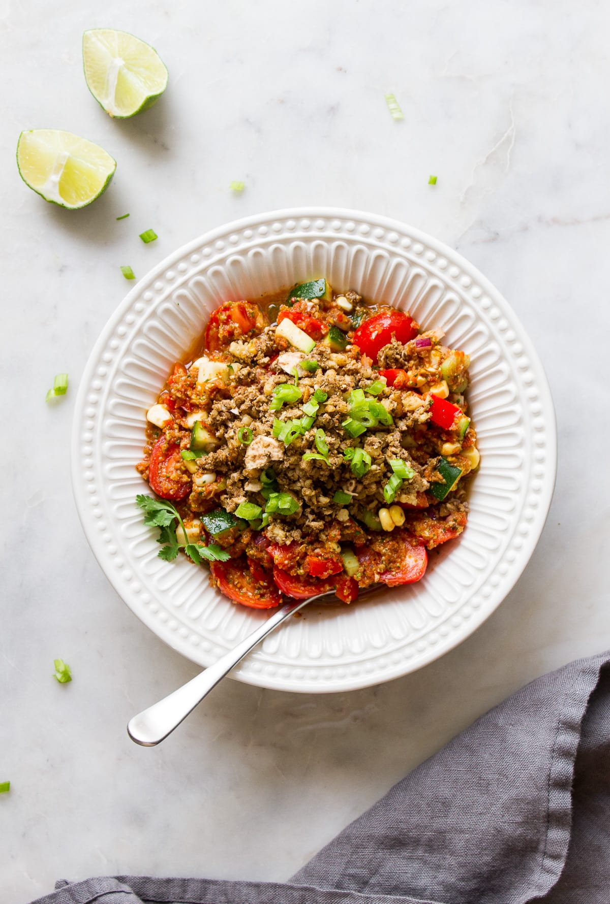 top down view of a serving of raw vegetable chili in a white bowl with spoon.