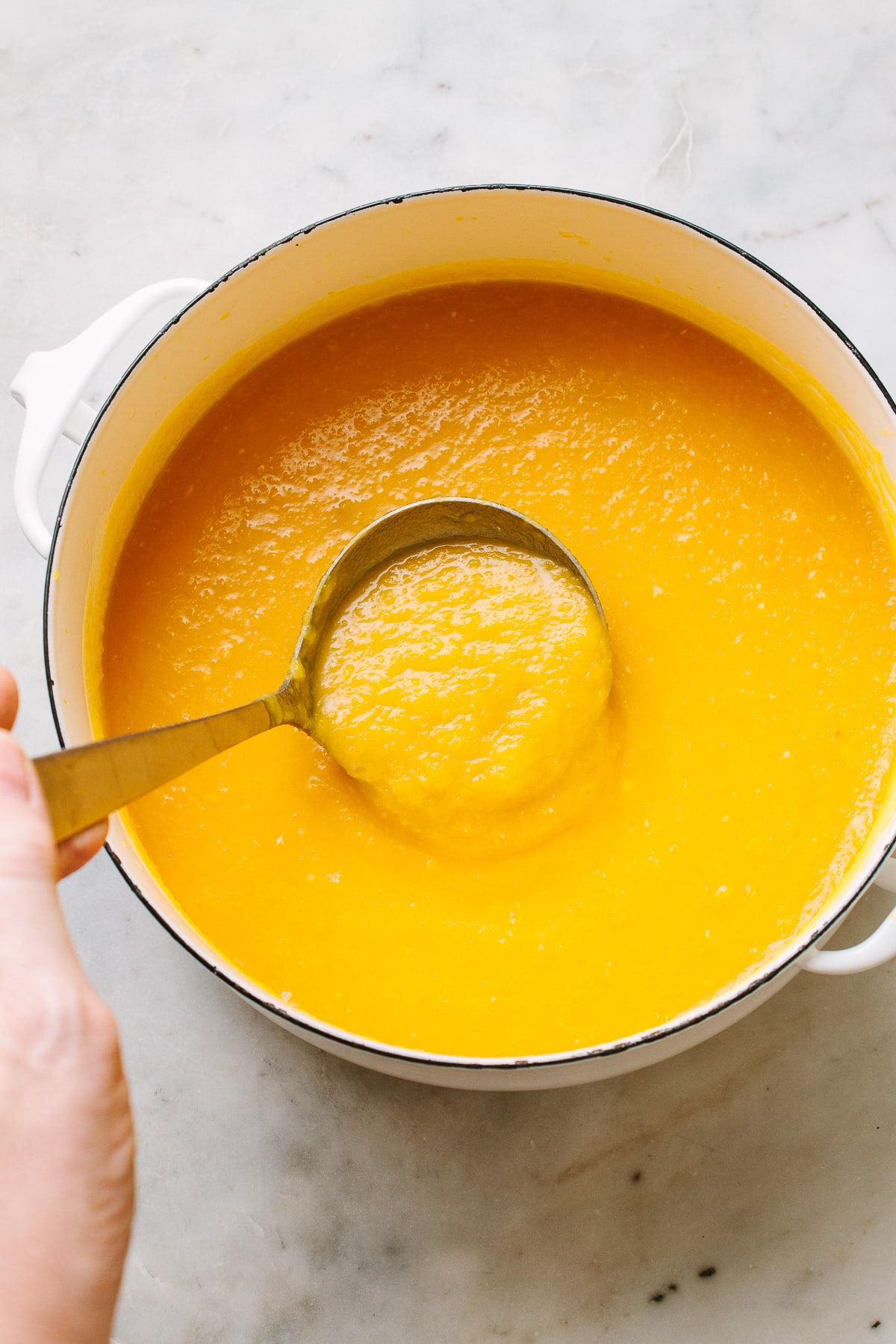 top down view of a pot with ladle filled with roasted butternut squash soup.