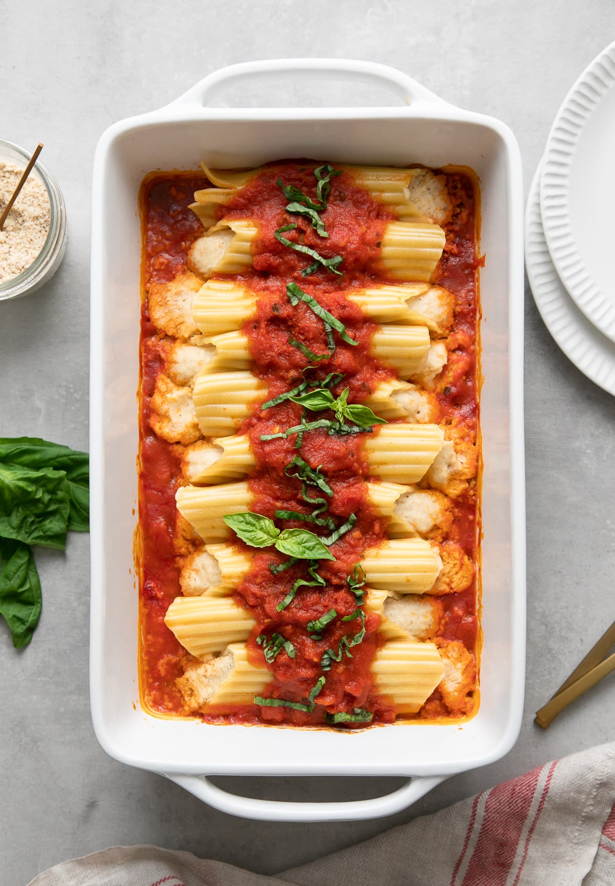 top down view of freshly baked vegan manicotti in a baking dish with items surrounding.