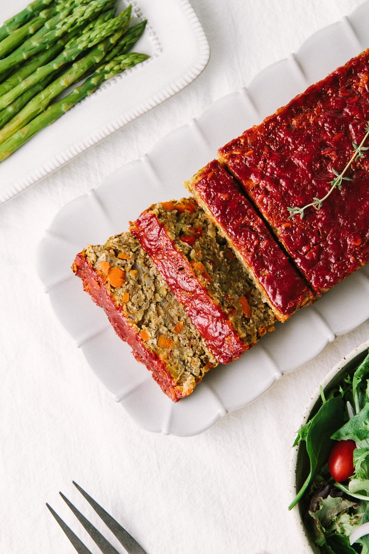 top down view of vegetable lentil loaf cut into slices on a serving platter surrounded by side dishes.