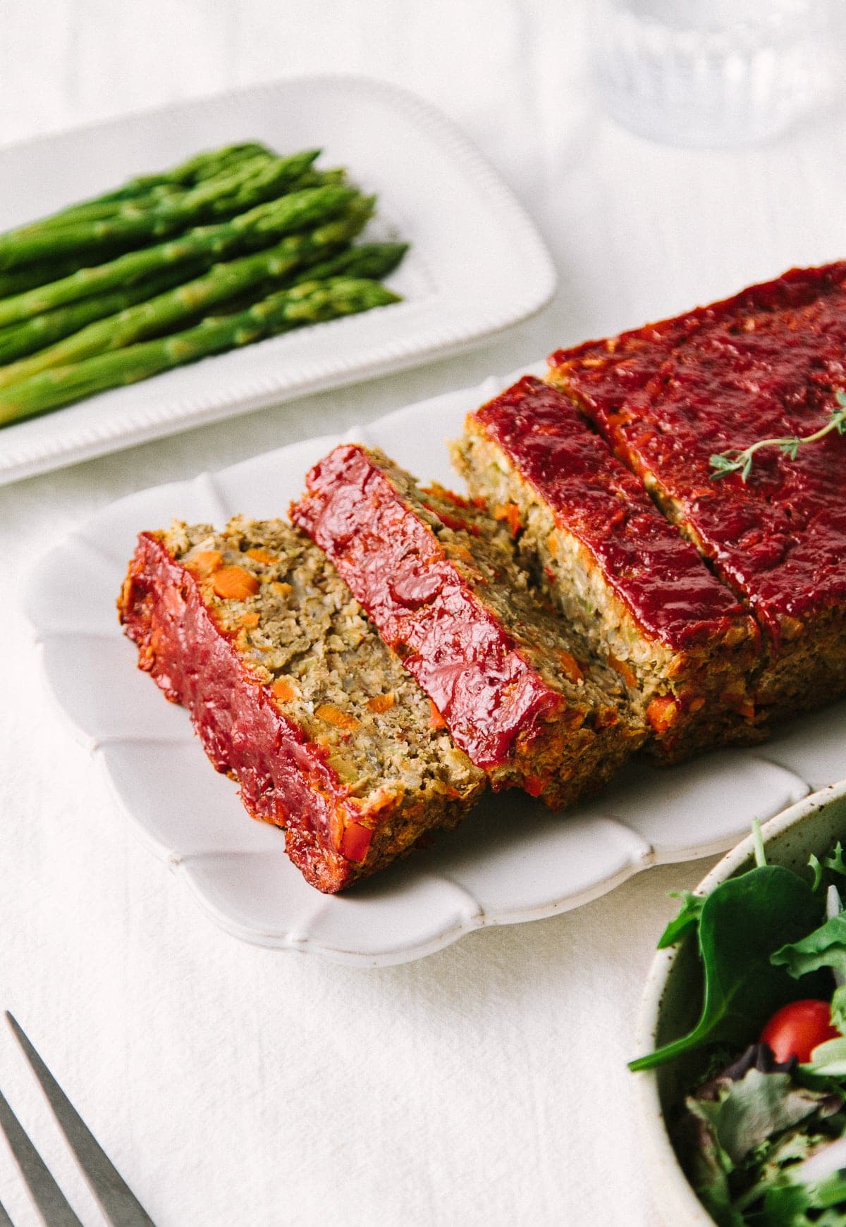 side angle view of vegetable lentil loaf cut into slices on a serving platter surrounded by side dishes.