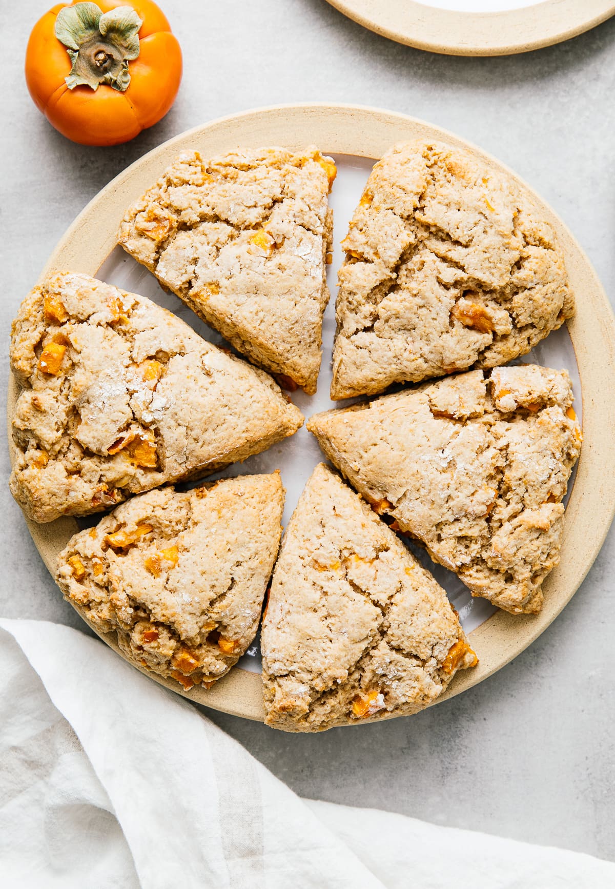 top down view of vegan persimmon ricotta scones on a plate with items surruonding.