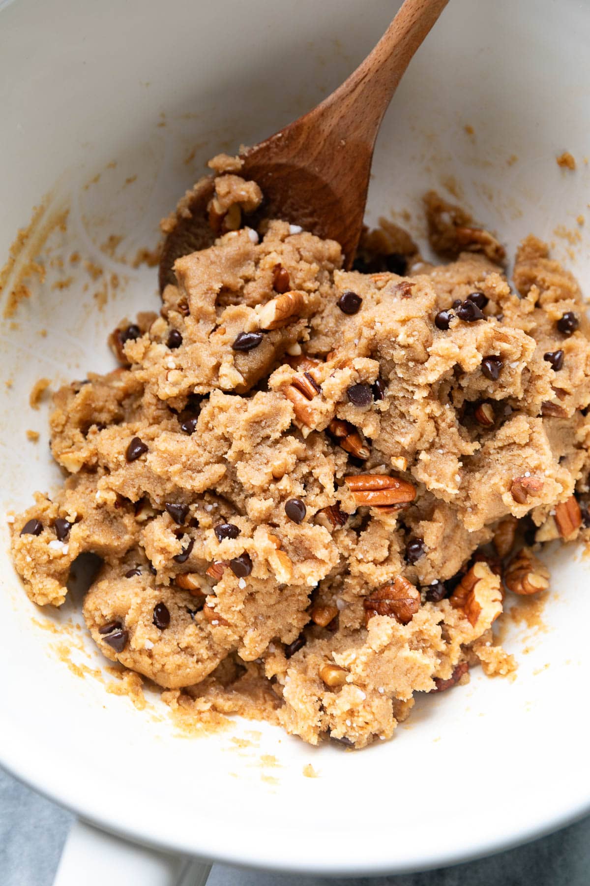 top down view of gluten free pecan cookie dough in a white mixing bowl with wooden spoon.