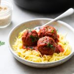 side angle view of a serving of vegan meatballs and marinara sauce overtop spaghetti squash in a bowl with fork.
