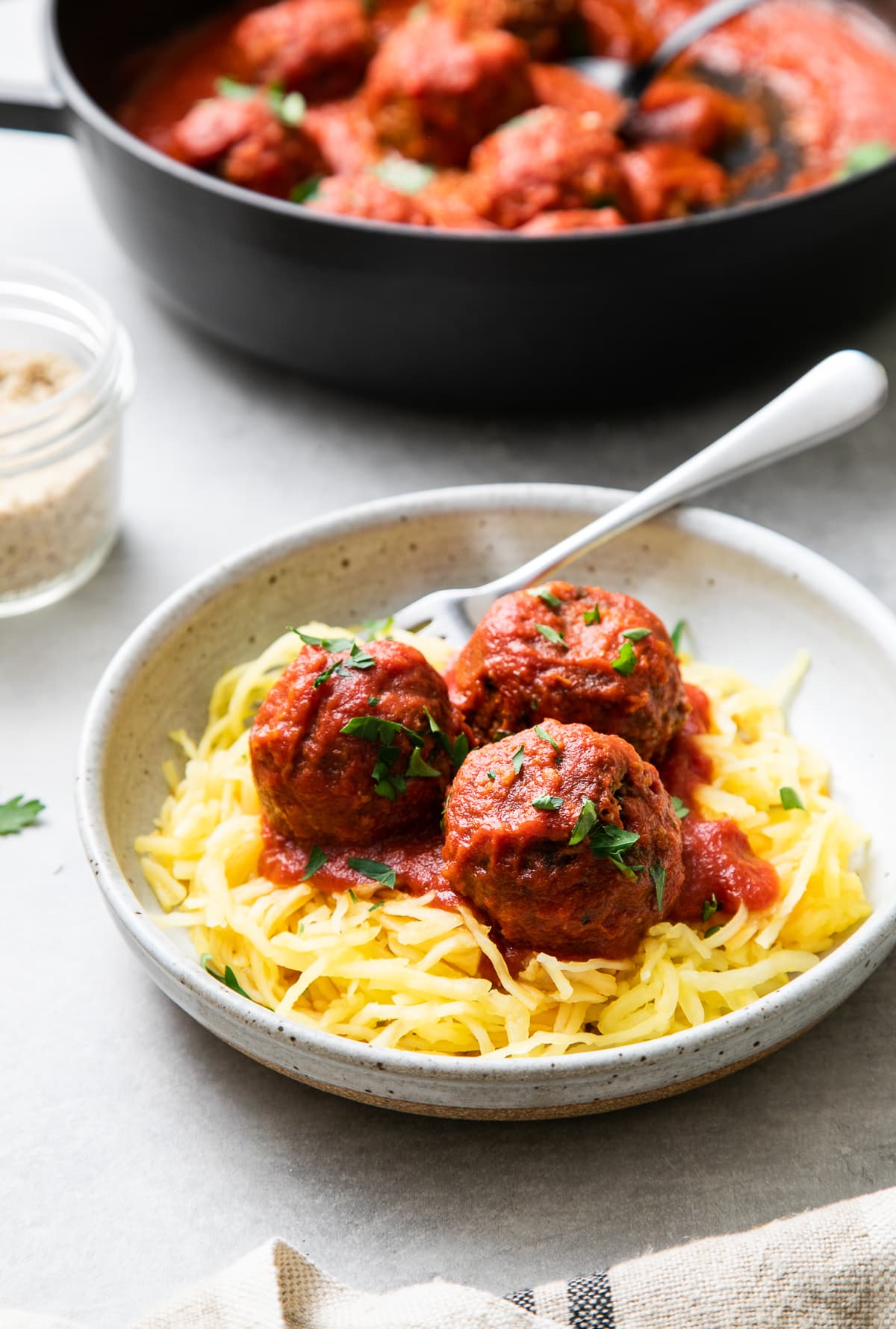 side angle view of a serving of vegan meatballs and marinara sauce overtop spaghetti squash in a bowl with fork.