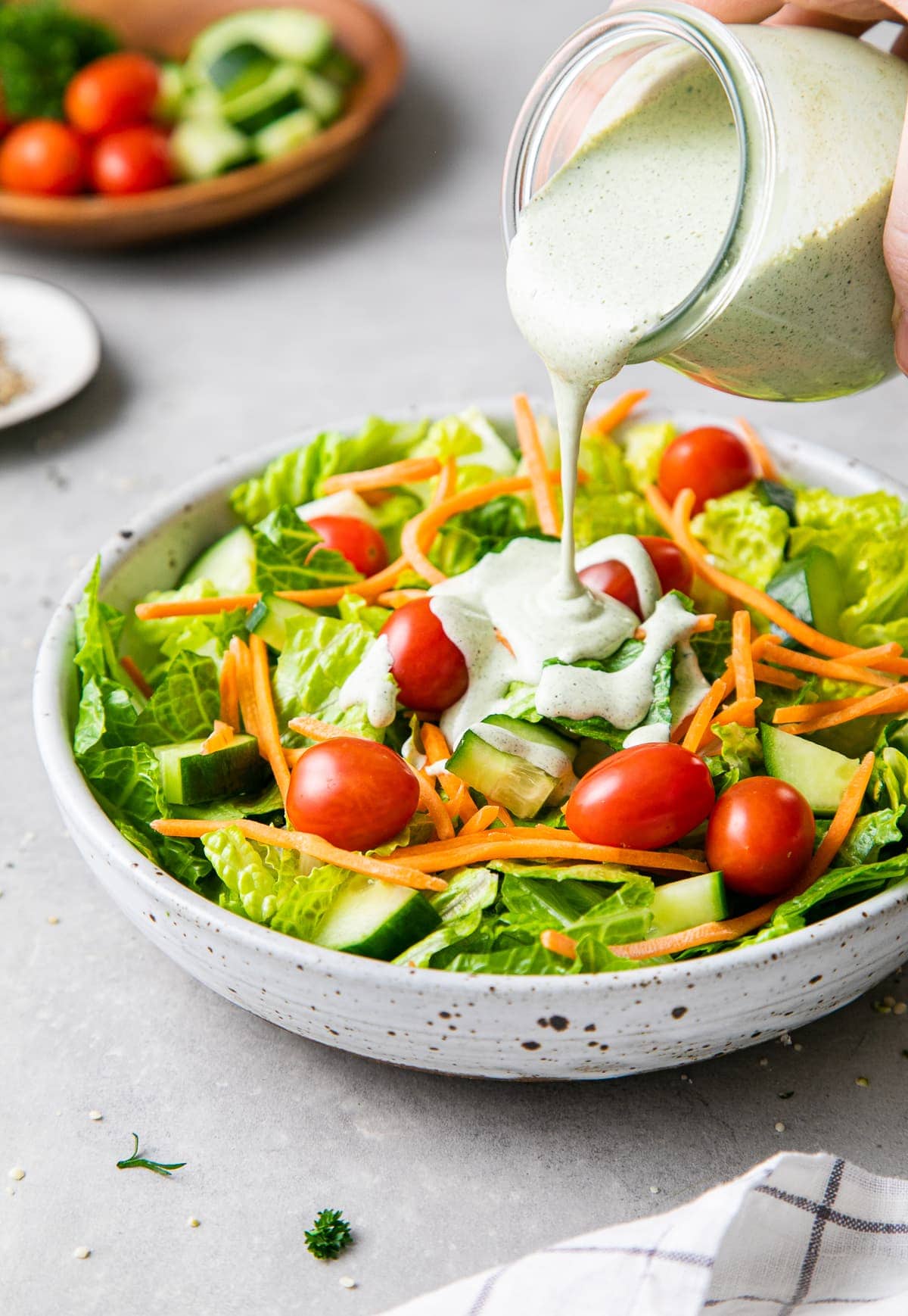 side angle view ranch style hemp seed dressing being poured over fresh green salad.