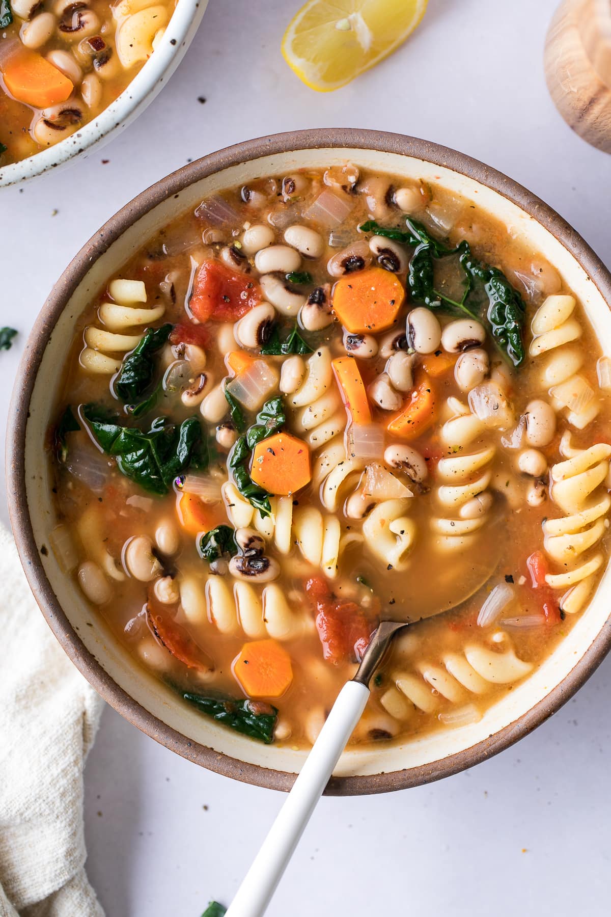 top down view of bowl of hearty pasta and bean soup with items surrounding.