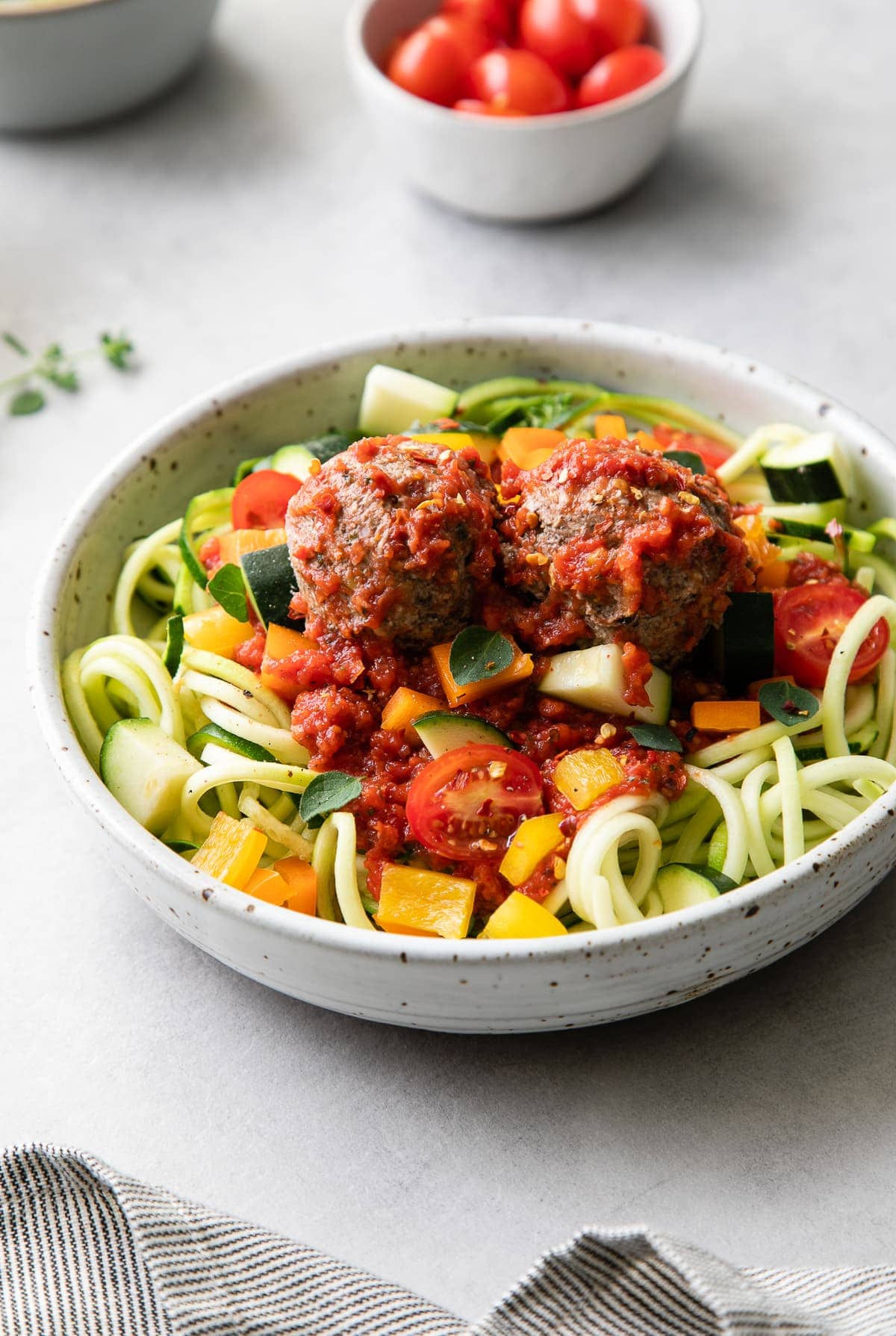 side angle view of bowl of raw pasta primavera with meatballs.