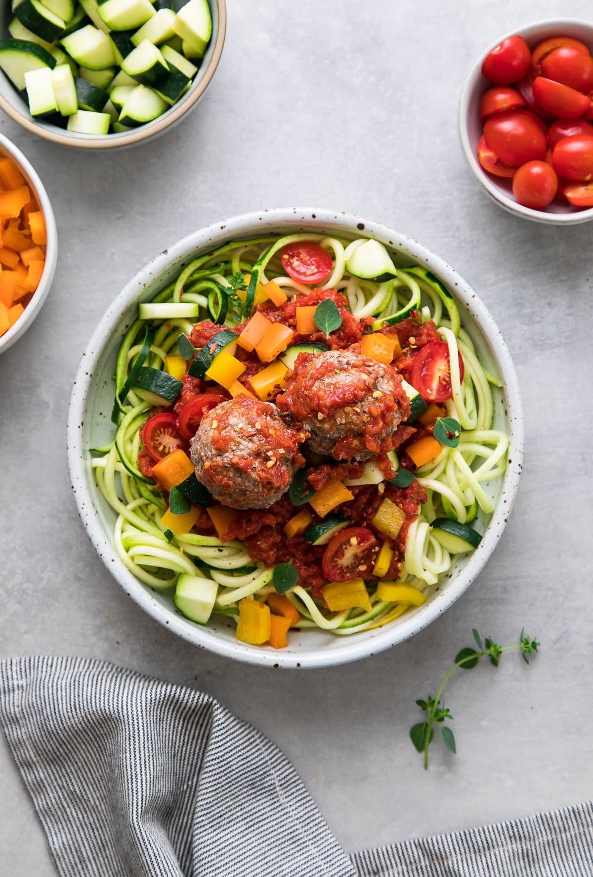 top down view of bowl of raw pasta primavera with meatballs.