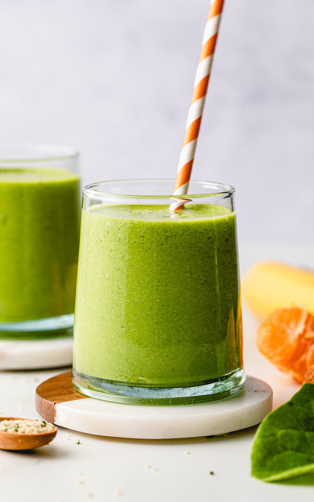 head on view of fresh green hemp smoothie in a glass with items surrounding.