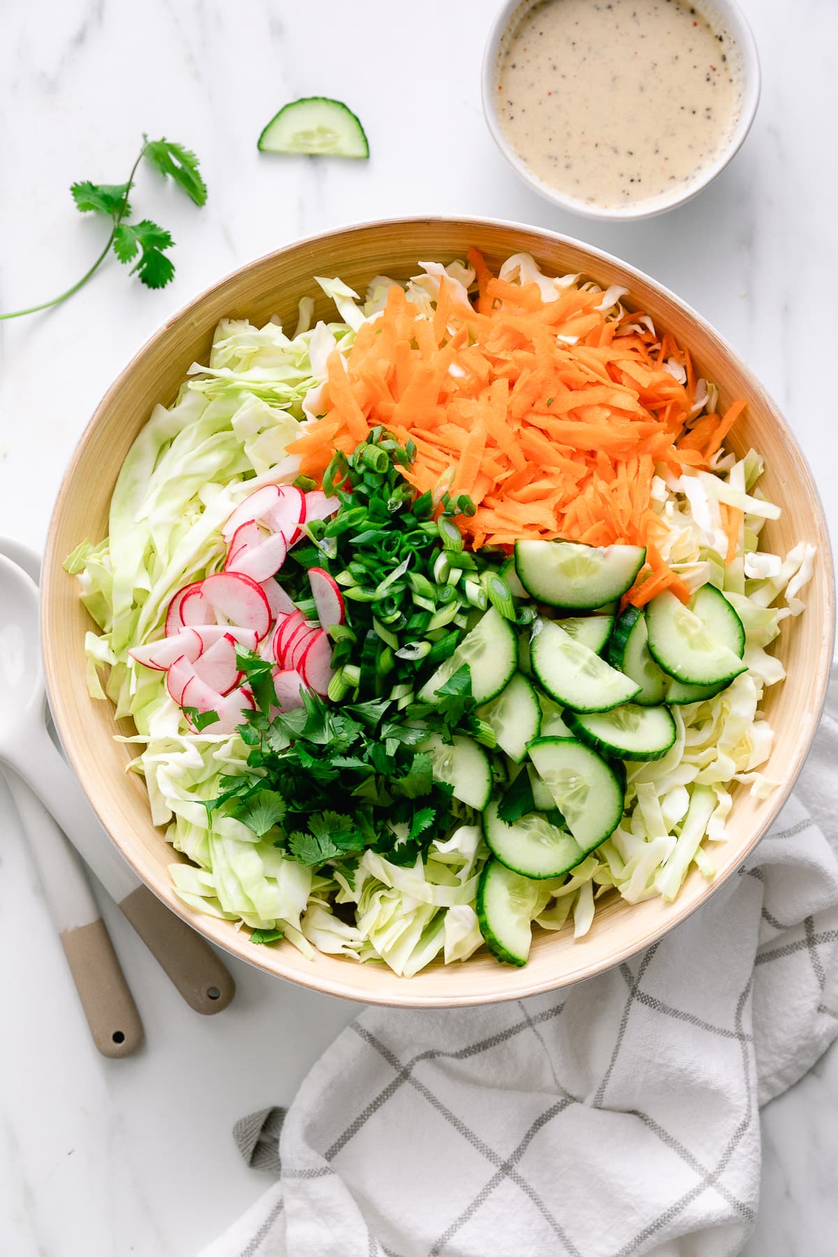 top down view of cabbage salad ingredients in large bowl with dressing on the side.