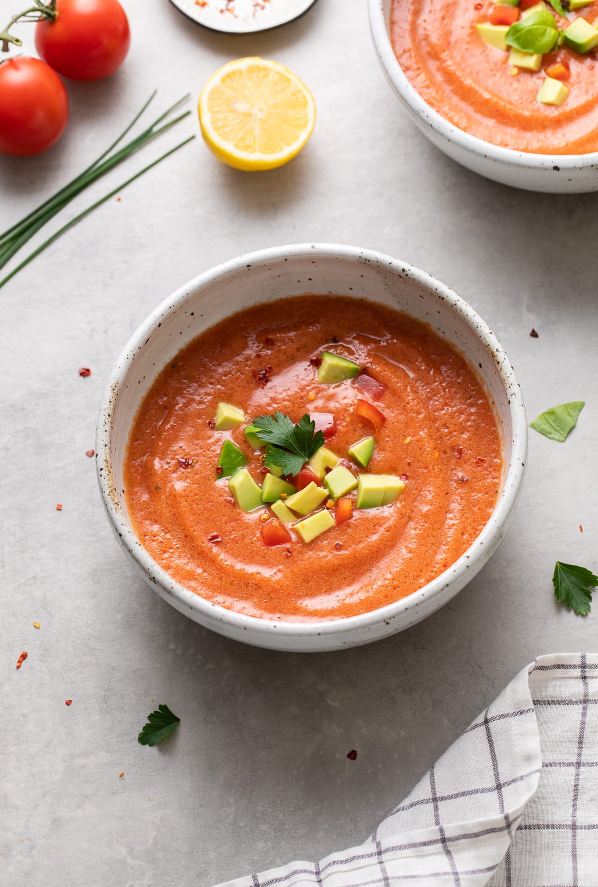 side angle view of bowl with serving of spicy raw tomato soup with items surrounding.