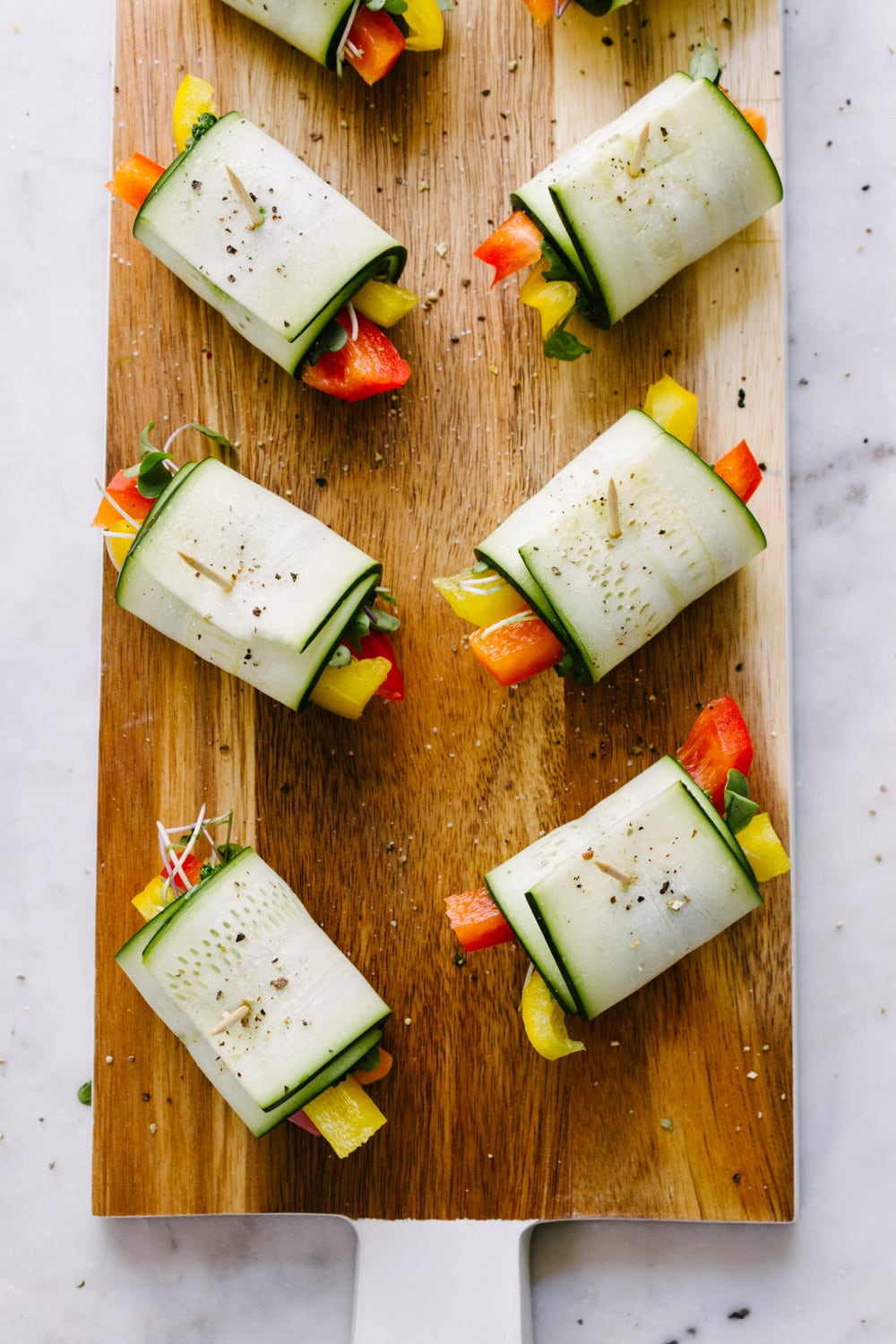 a top down view of a group of raw zucchini wraps filled with fresh bell peppers, carrots, kale pesto and micro greens freshly made and sitting on a wooden serving board