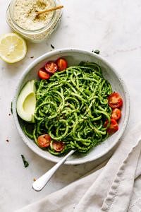 a top down view of a bowl of zucchini noodles tossed with spicy kale pesto and avocado and fork