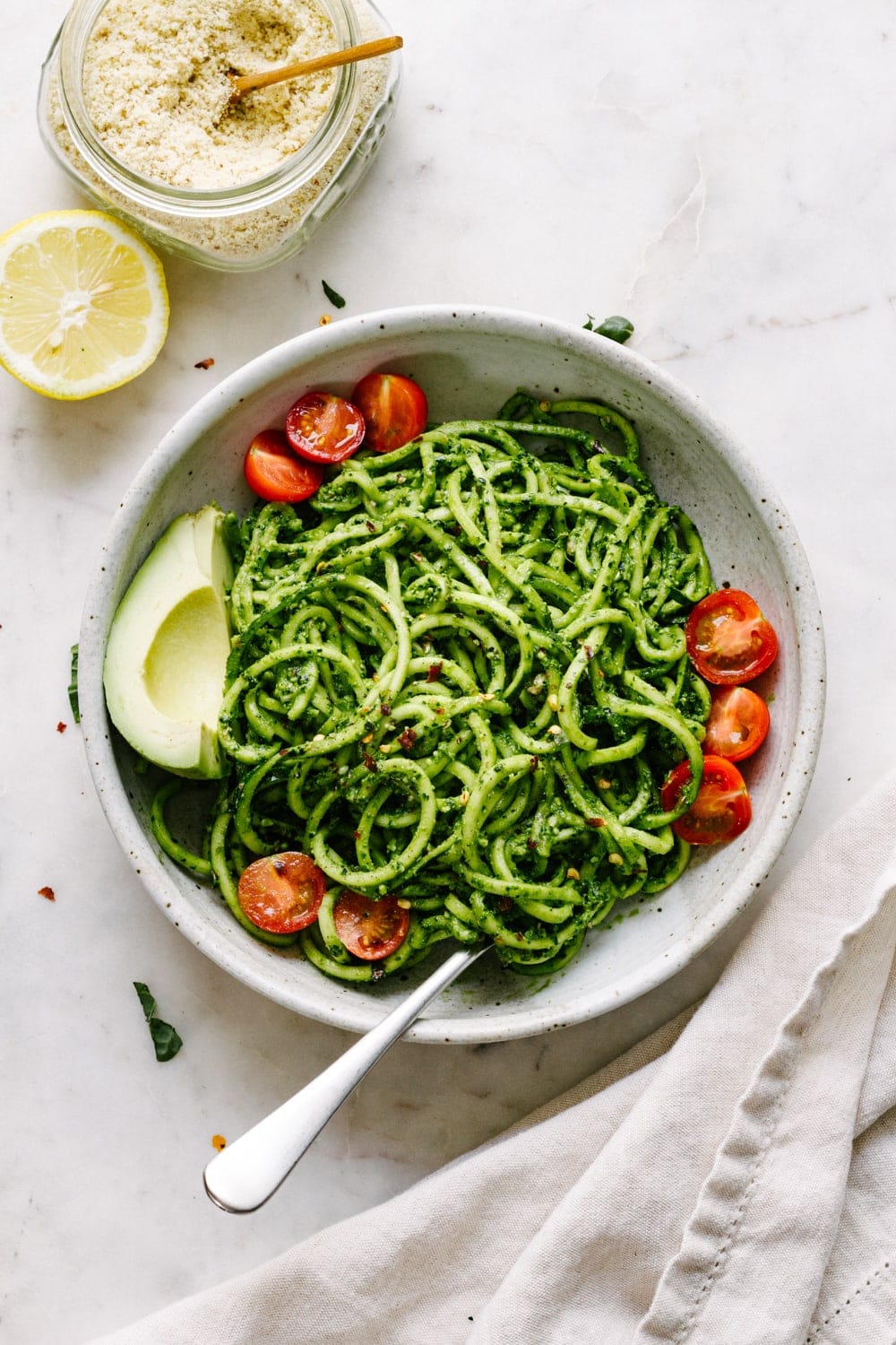 a top down view of a bowl of zucchini noodles tossed with spicy kale pesto and avocado and fork