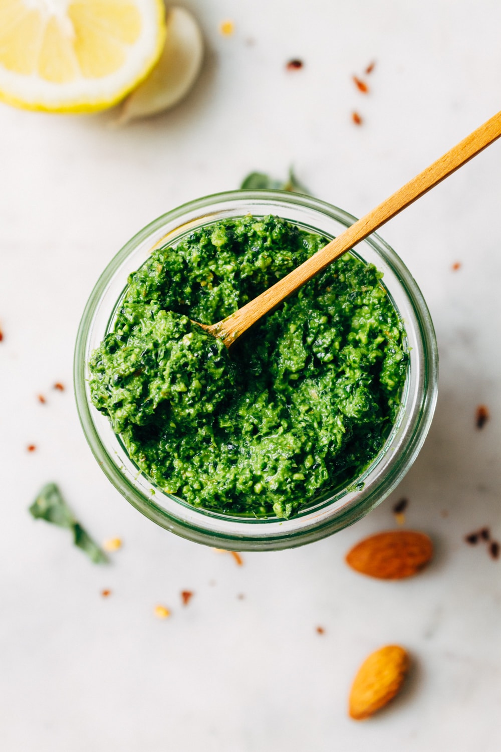top down view of spicy vegan kale pesto in a glass jar with wooden spoon