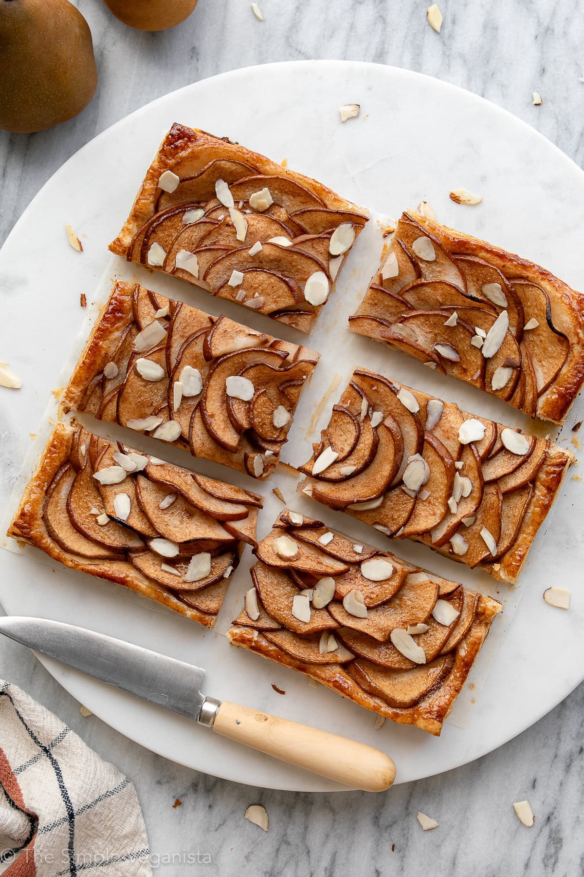 Freshly baked vegan pear tart cut into slices on a marble serving board.