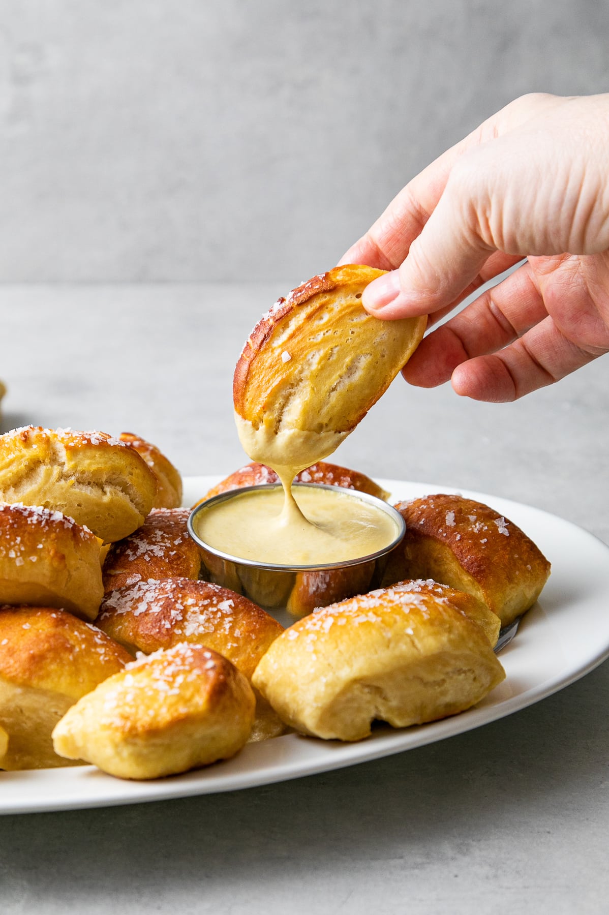 head on view of soft pretzel bite dipped in vegan queso with items surrounding.