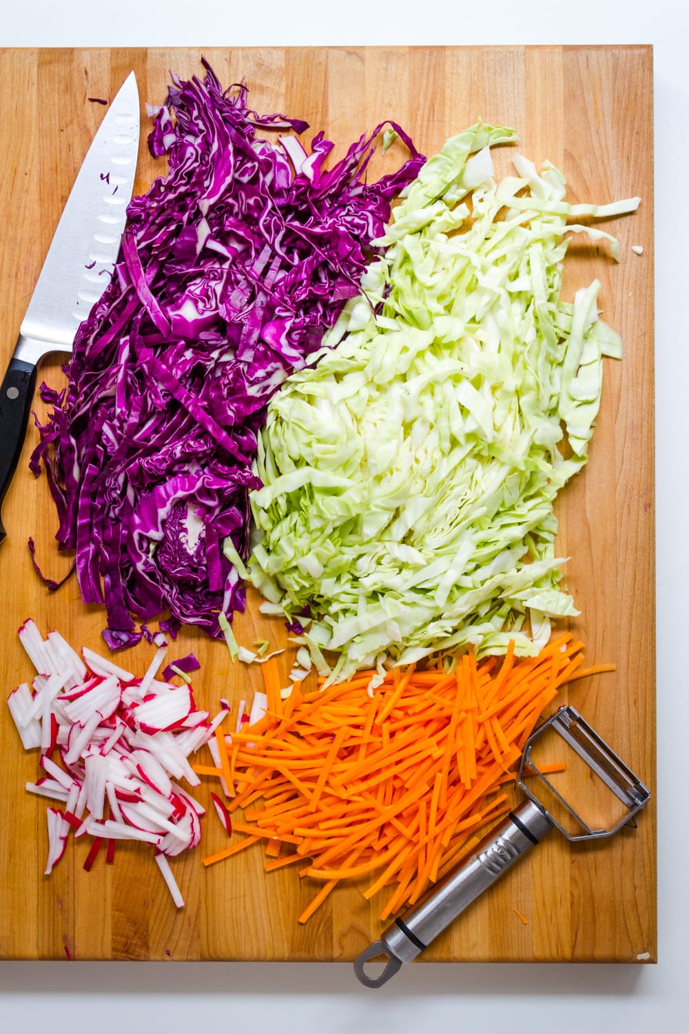 top down view of prepped ingredients for asian slaw salad on a wooden cutting board.