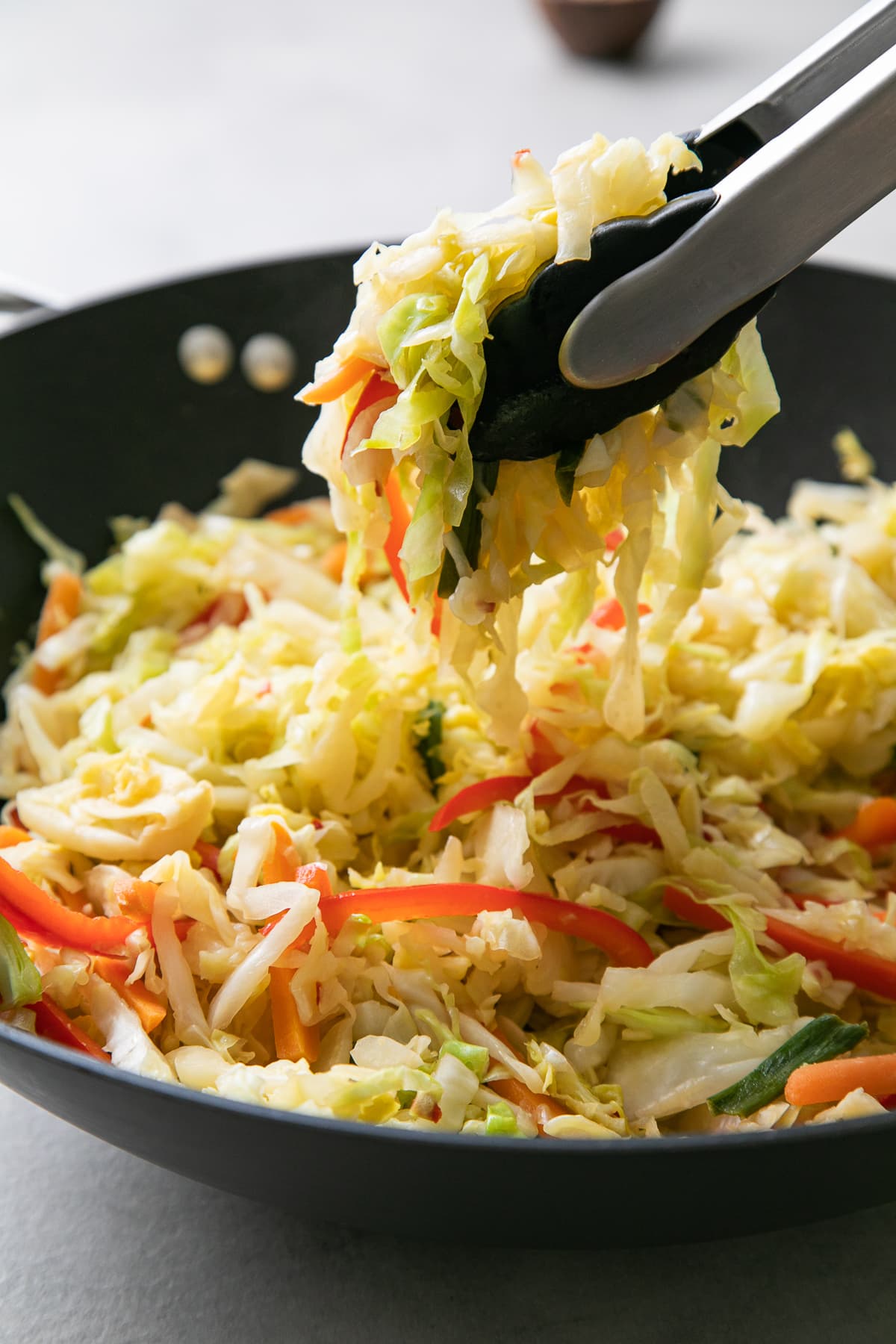 side angle view of cabbage stir fry picked up with tongs in pan.