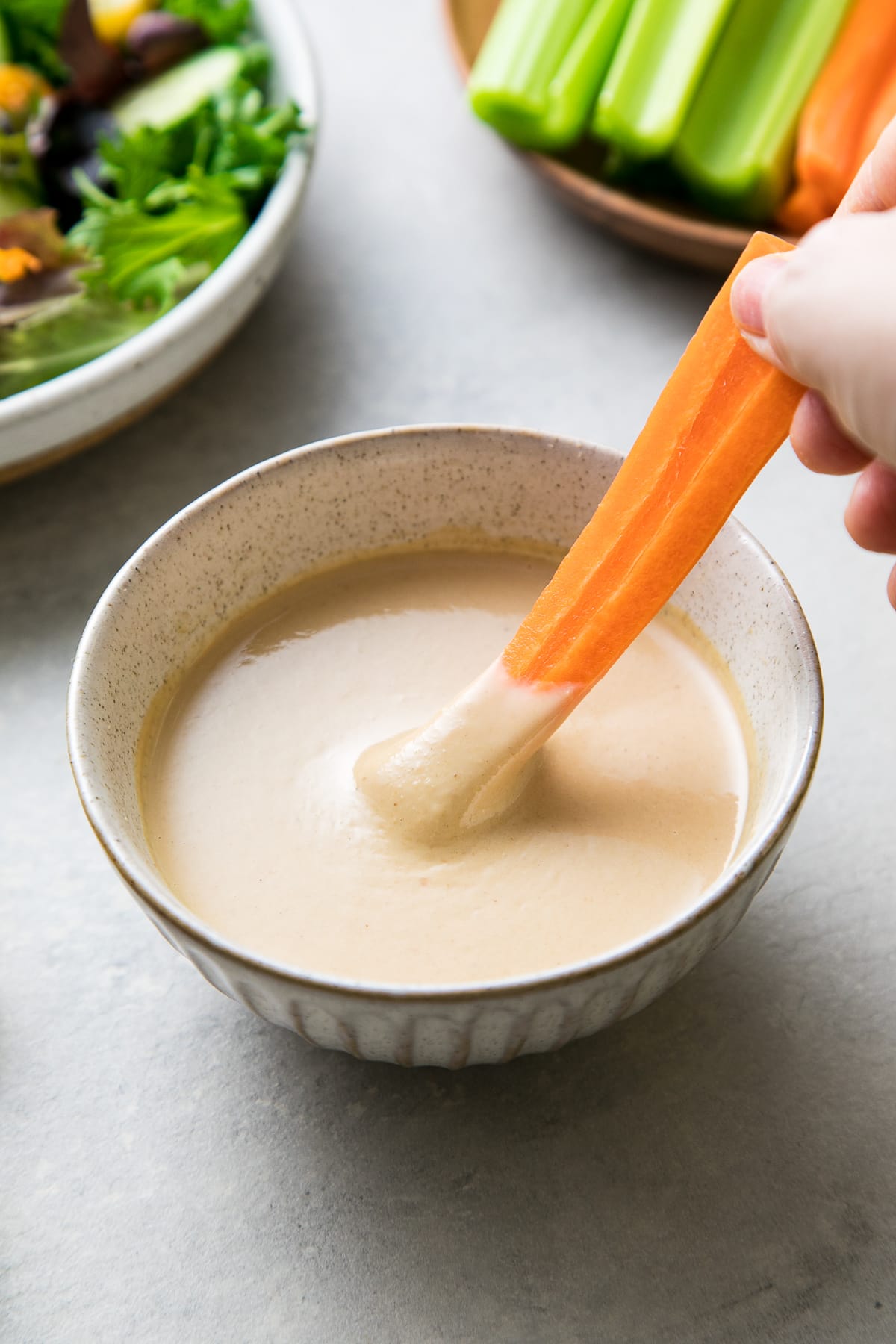 side angle view of carrot being dipped into healthy tahini miso dip.