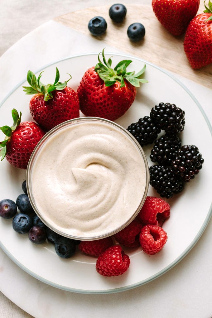 top down view of a small white plate with berries and small glass bowl filled with cashew sweet cream.
