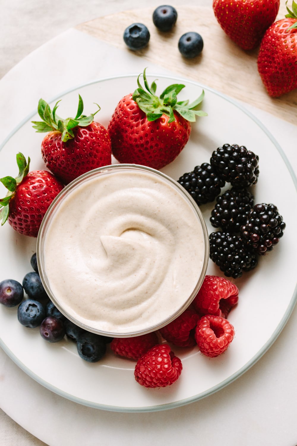 top down view of a small white plate with berries and small glass bowl filled with cashew sweet cream.