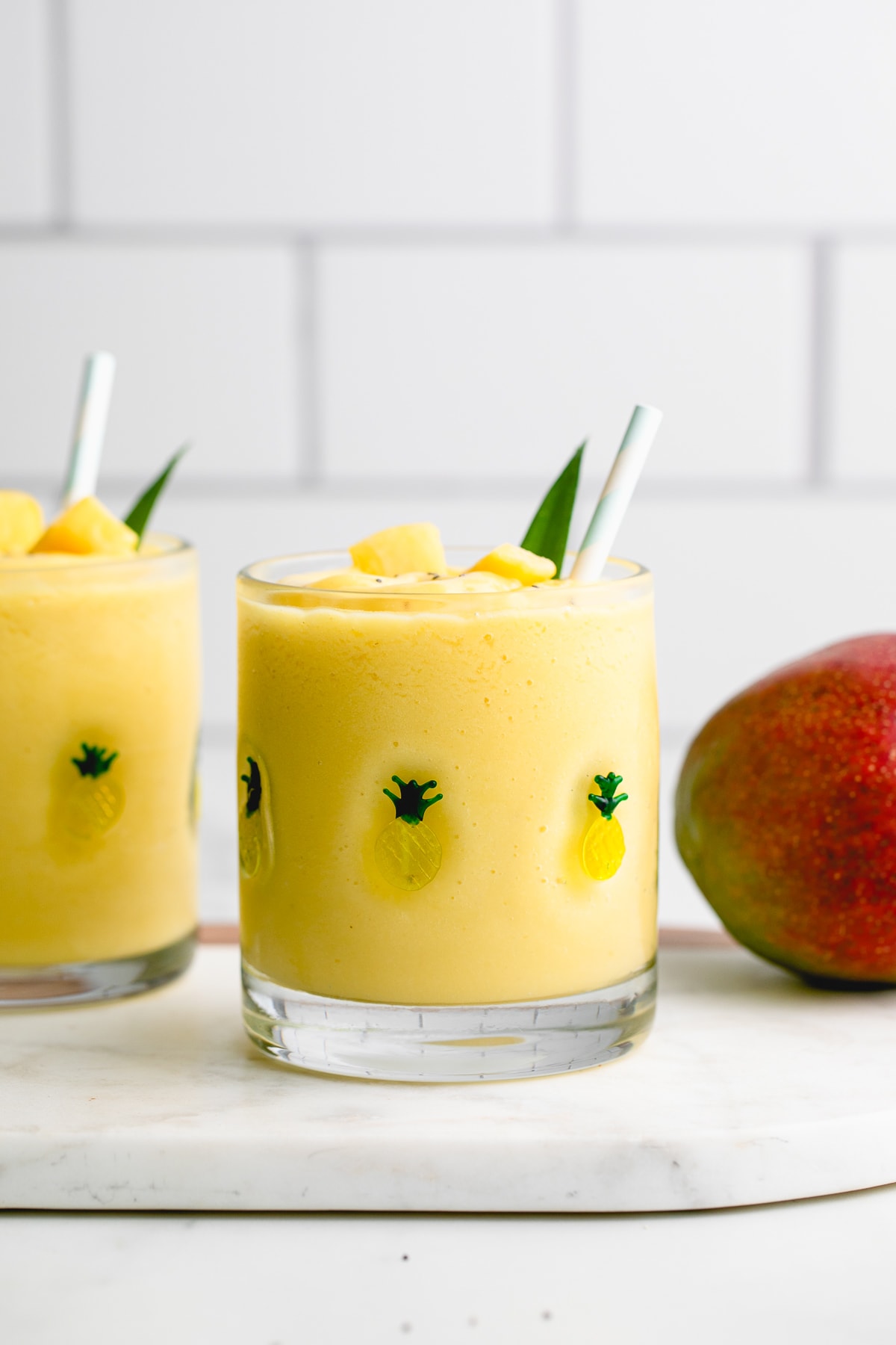 head on view of pineapple mango banana smoothie in a glass with items surrounding.