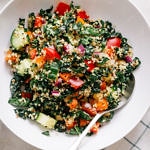 top down view of kale and quinoa salad in a white bowl with spoon and lemon wedge.
