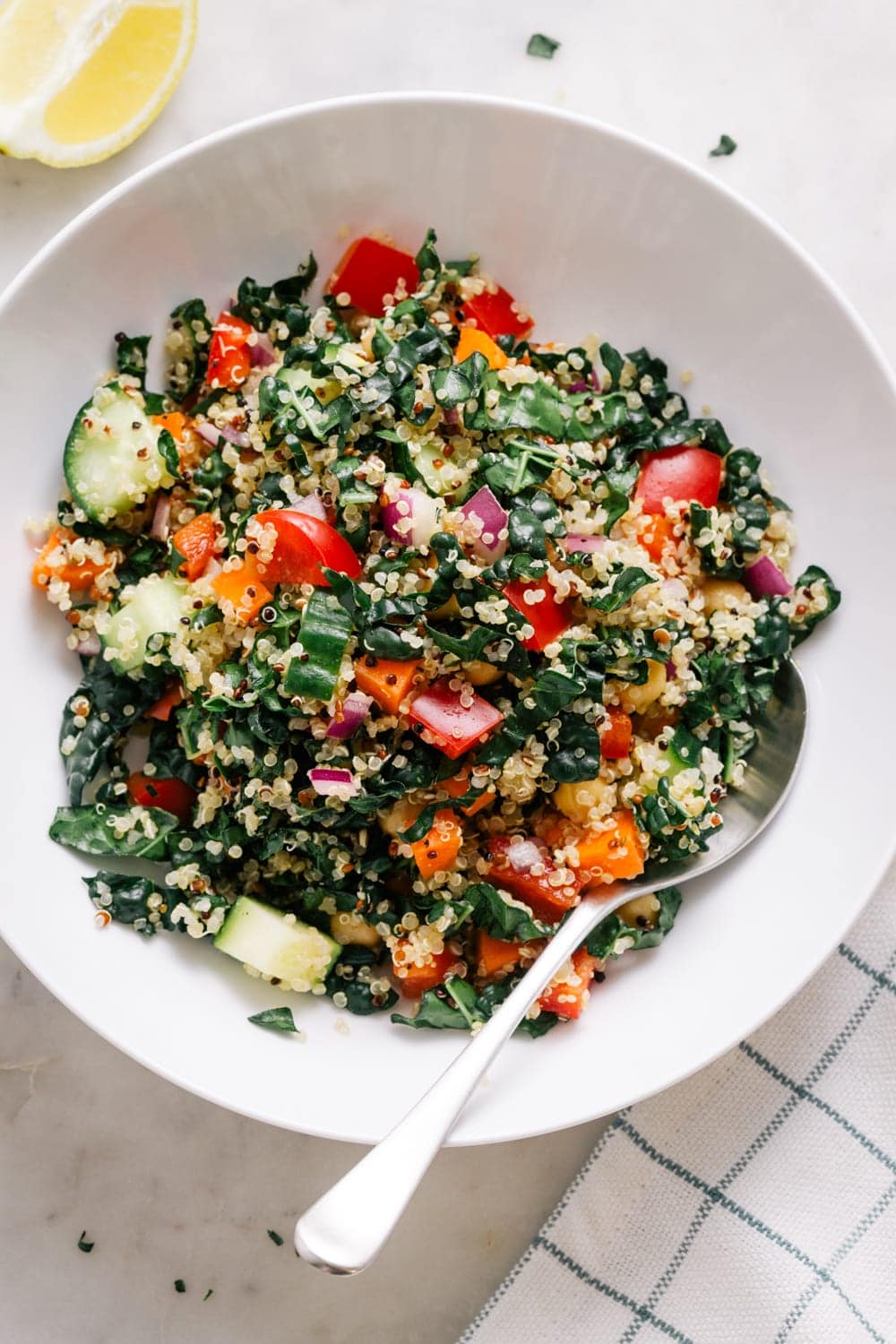 top down view of kale and quinoa salad in a white bowl with spoon and lemon wedge.