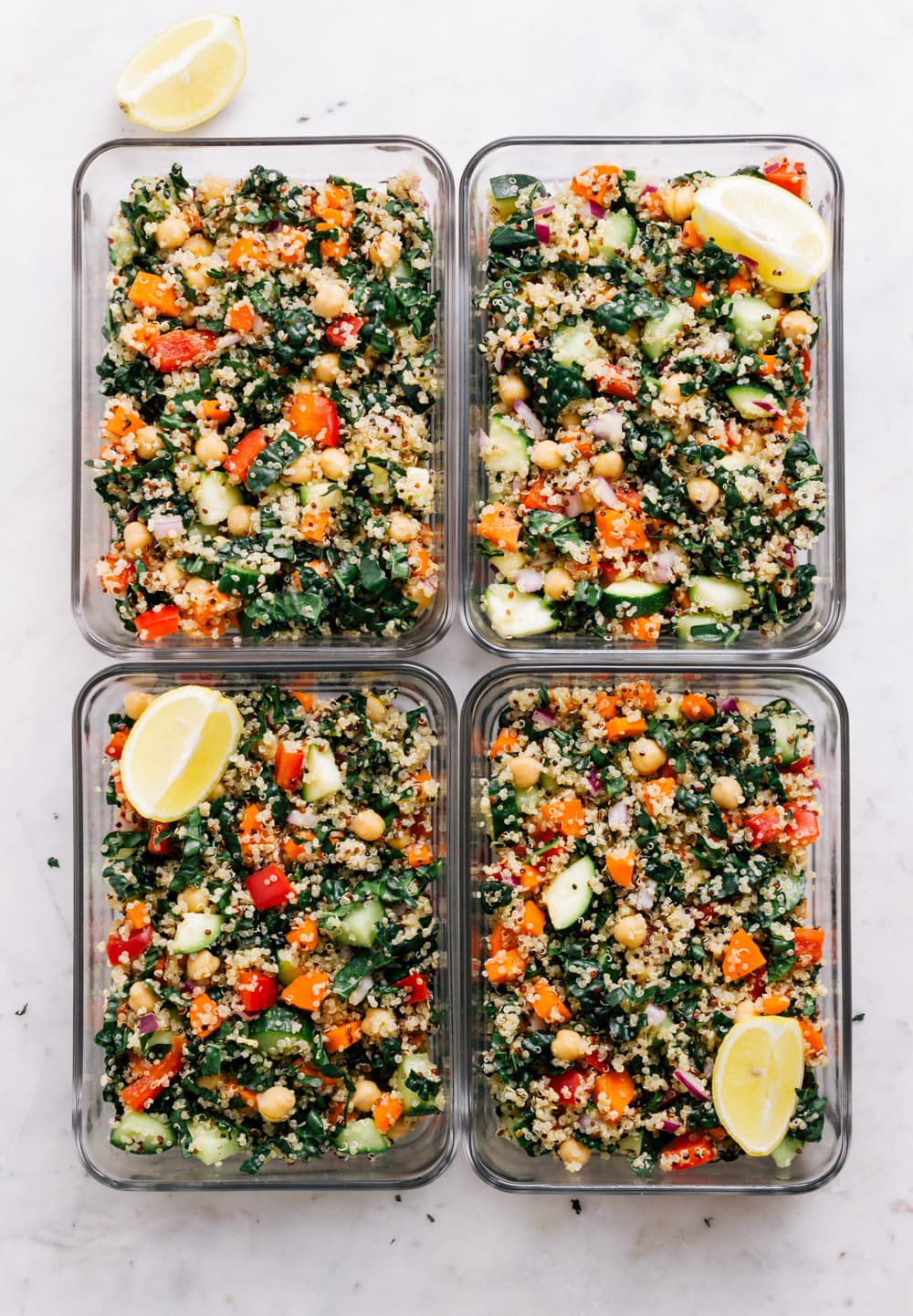 top down view of 4 meal prep containers filled with kale and quinoa salad with lemon wedge.