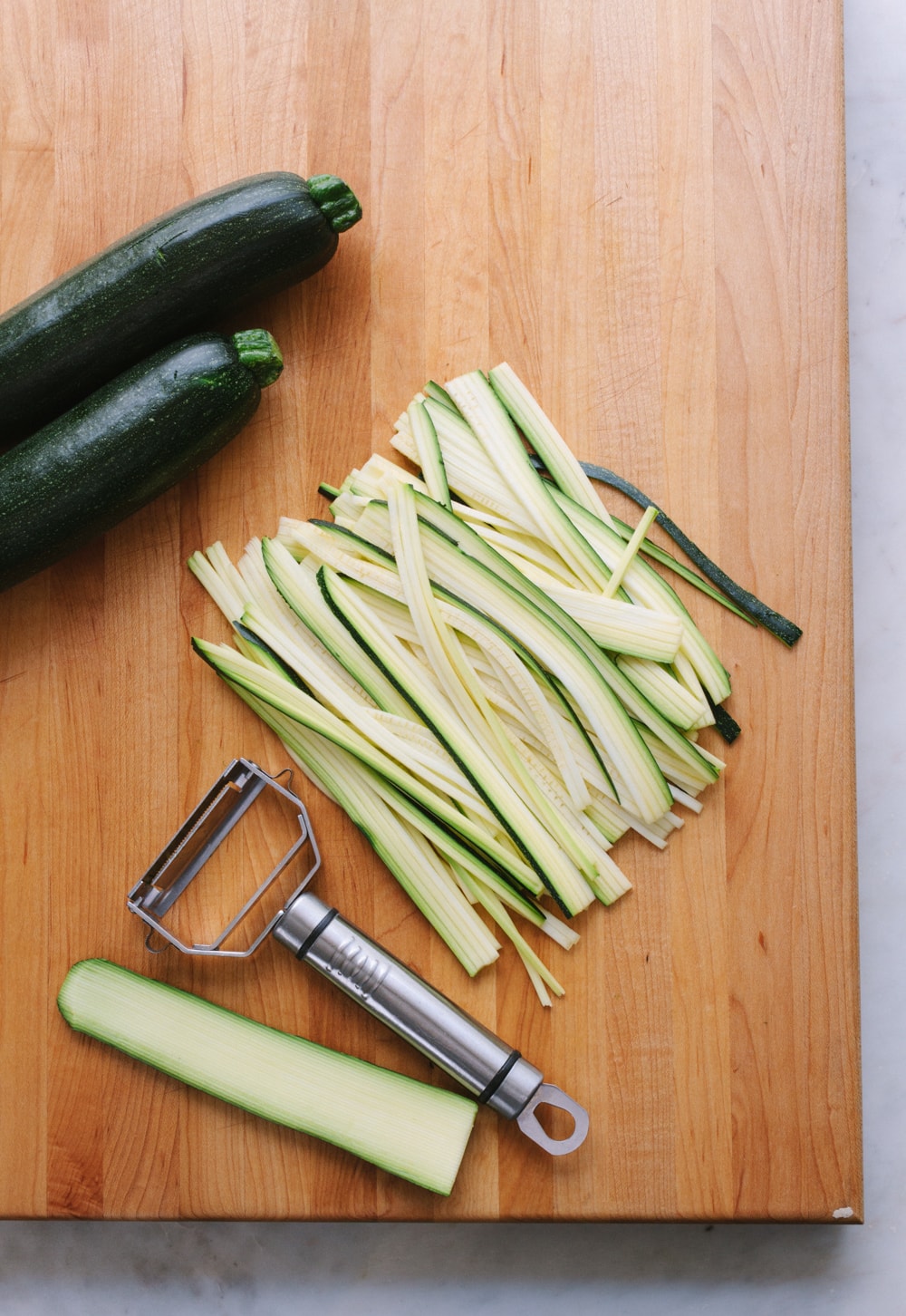 top down view of zucchini made into zucchini pasta noodles using a julienne tool on a wooden cutting board