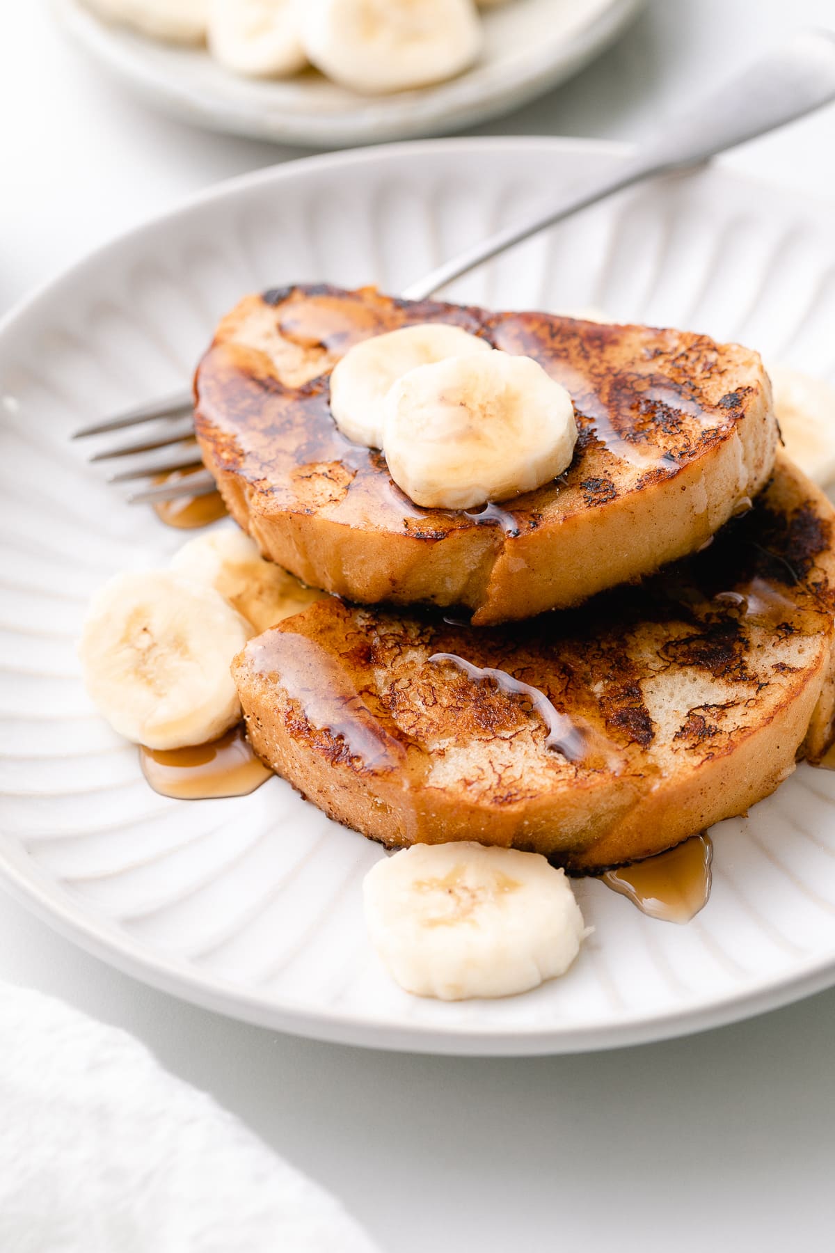 side angle view of vegan banana french toast on a plate with items surrounding.