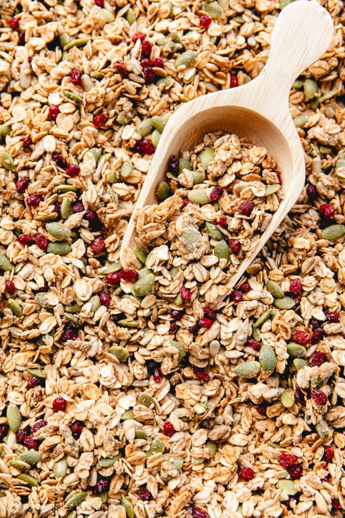 side angle view of freshly made granola on a rimmed baking sheet with wooden scoop.