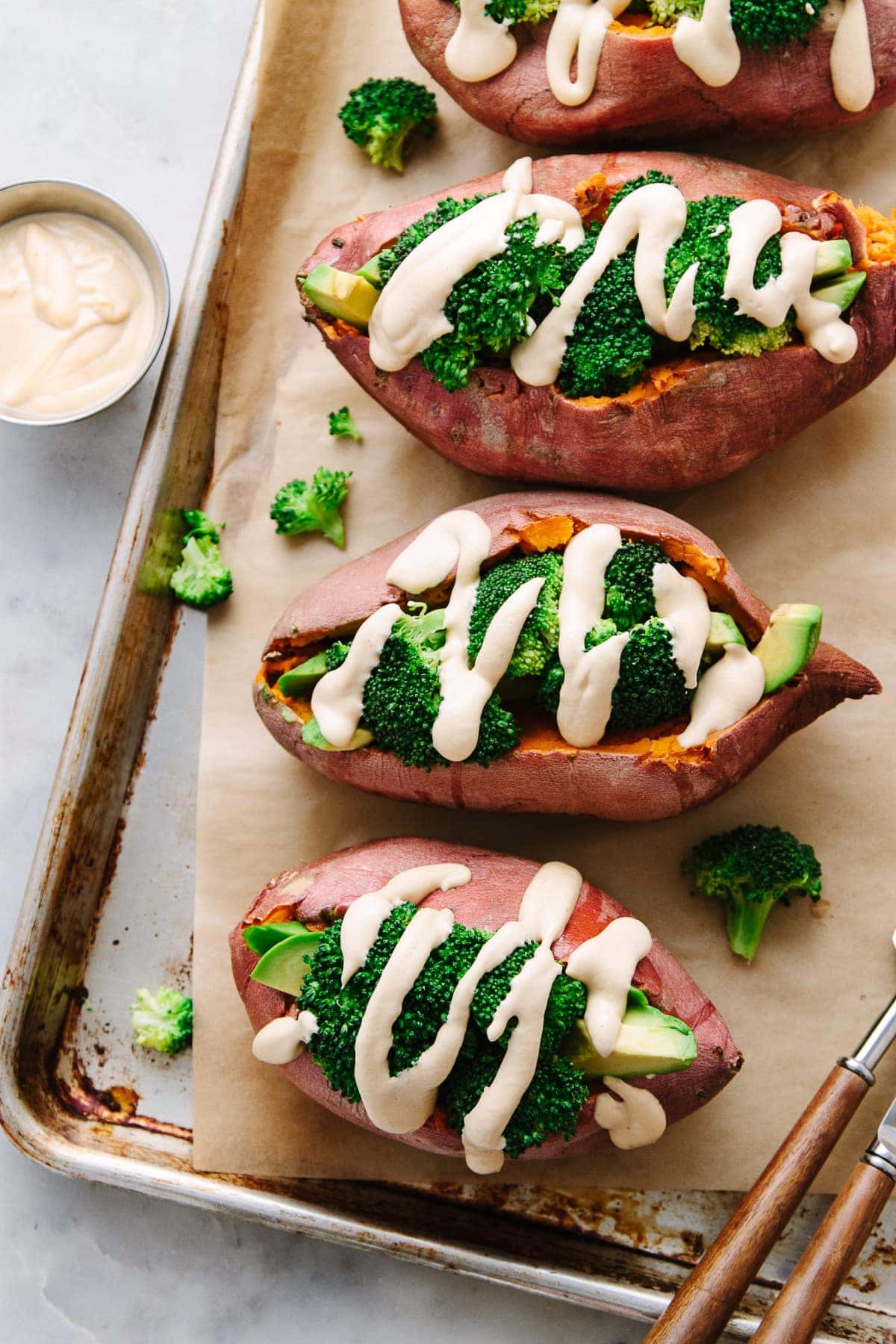 top down view of stuffed baked sweet potatoes with broccoli, avocado and creamy spice cheese sauce on a baking sheet.