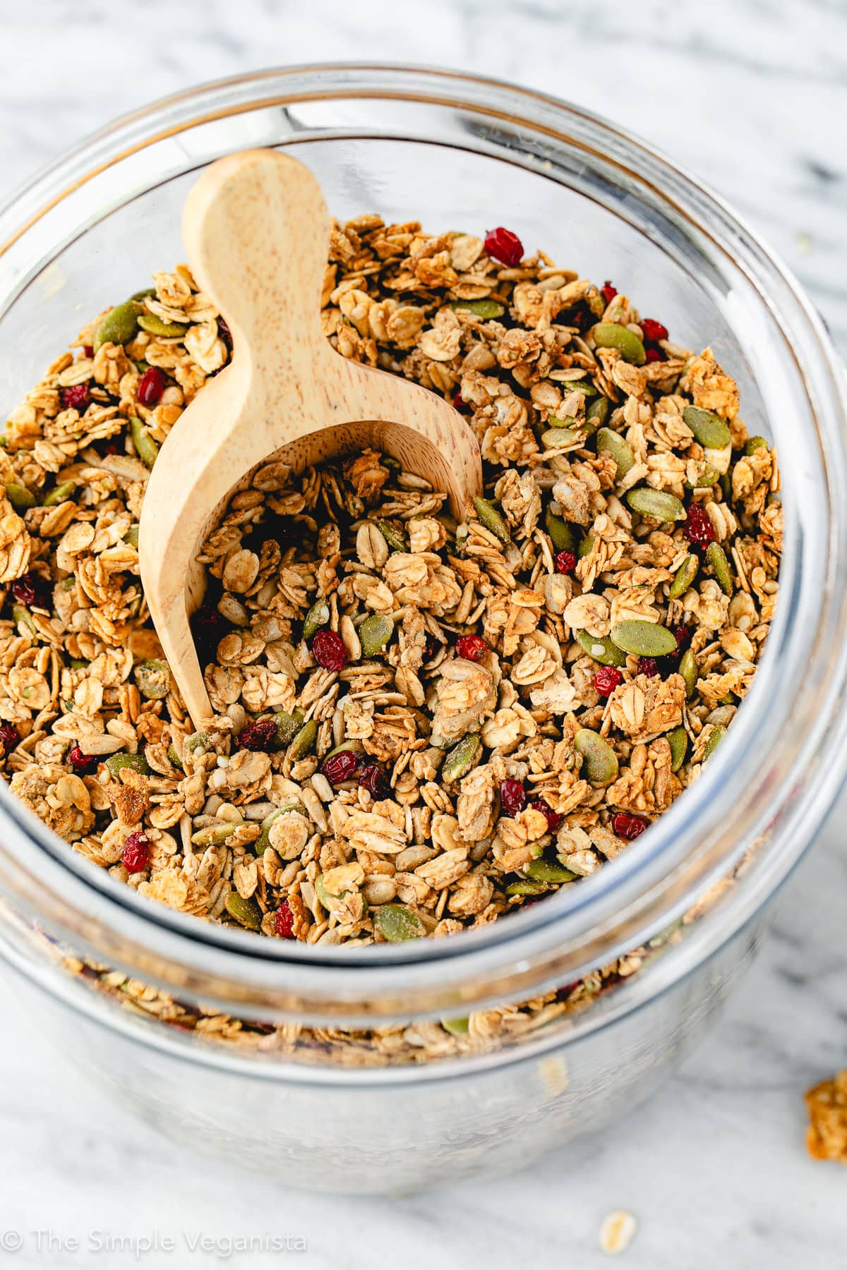 side angle view of homemade granola in a glass jar with wooden scoop.