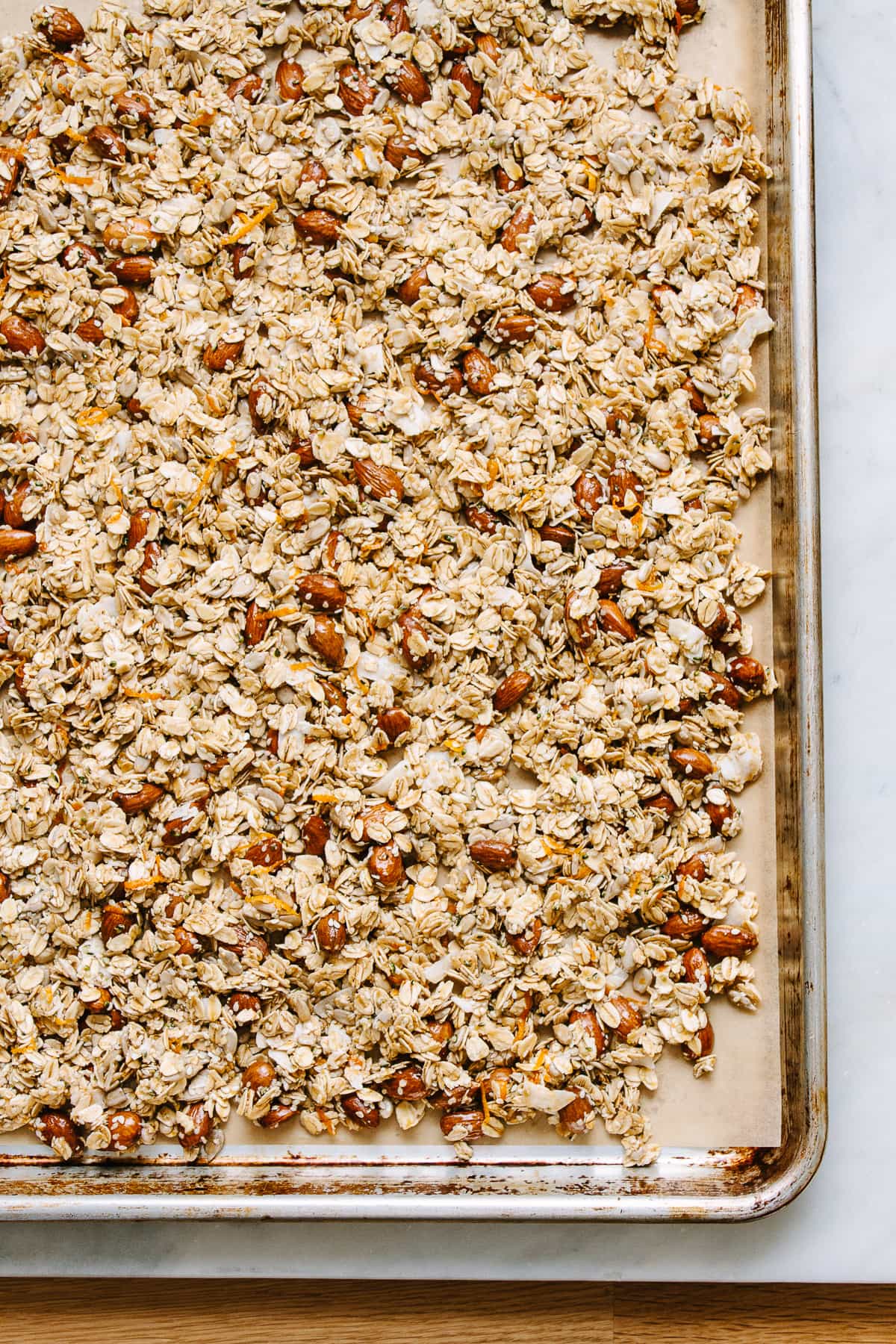 top down view of freshly mixed granola layered on a rimmed baking sheet before baking.