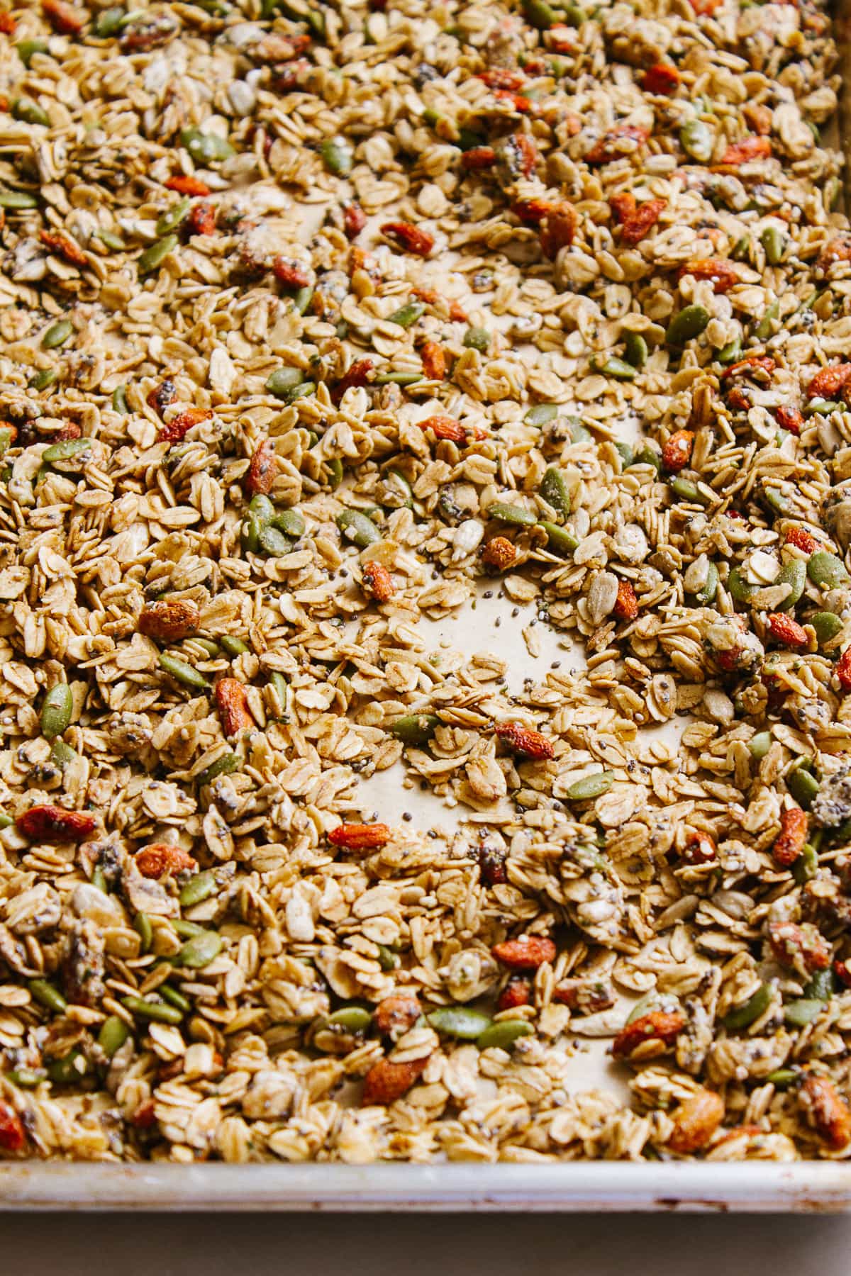 side angle view of freshly made seeds and goji berry granola on a baking sheet.