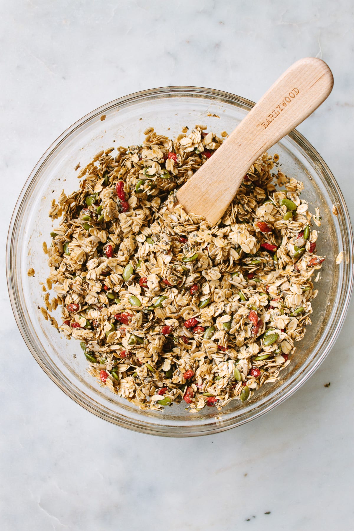 top down view of a glass mixing bowl with freshly mixed batch of seeds and goji berry granola.
