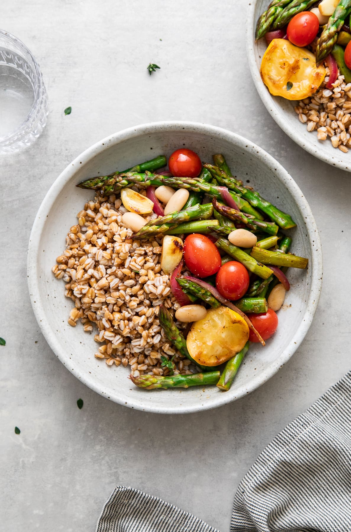 top down view of a bowl with serving of skillet asparagus and tomato medley with farro and items surrounding.