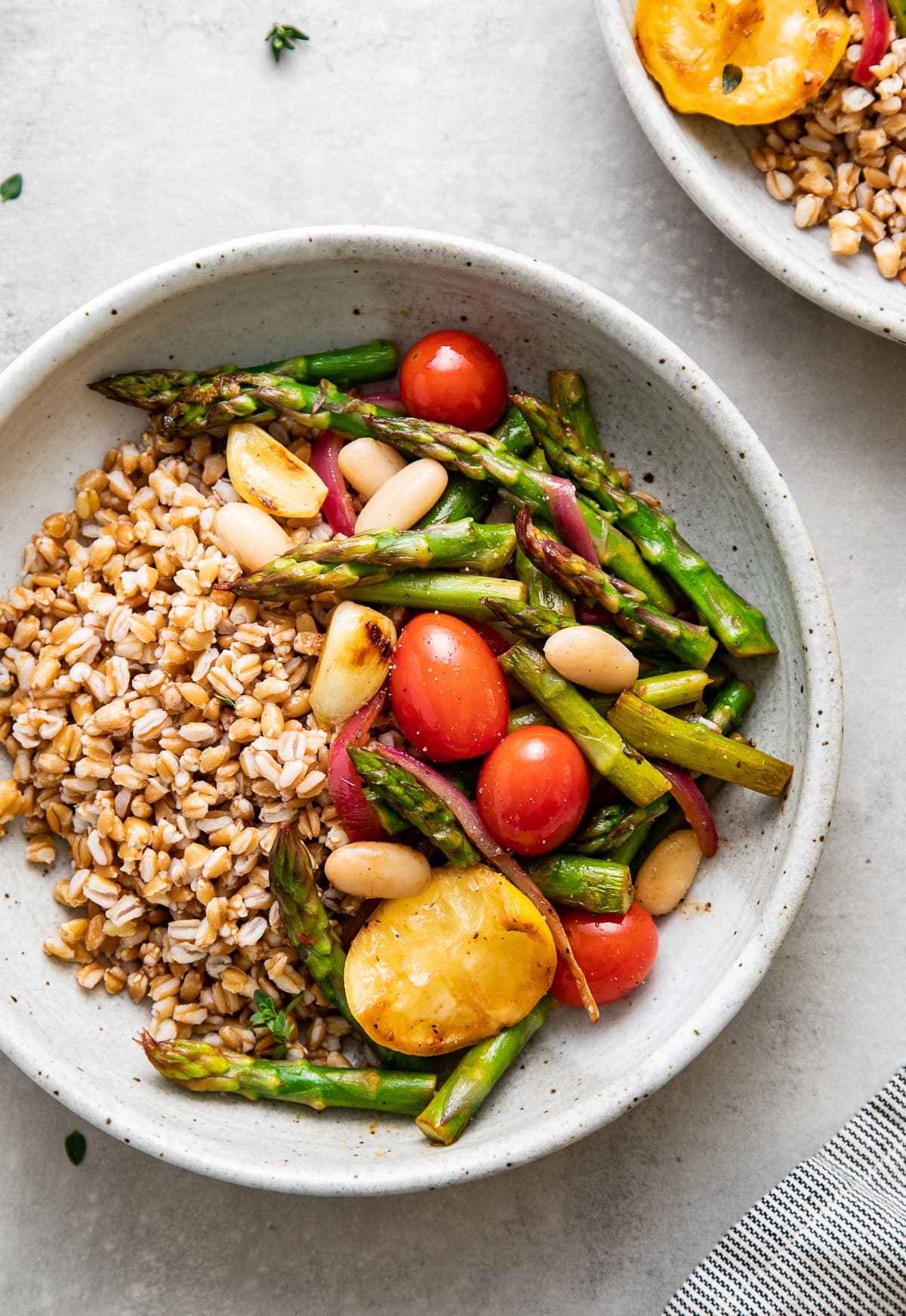 up close, top down view of a bowl with serving of skillet asparagus and tomato medley with farro and items surrounding.