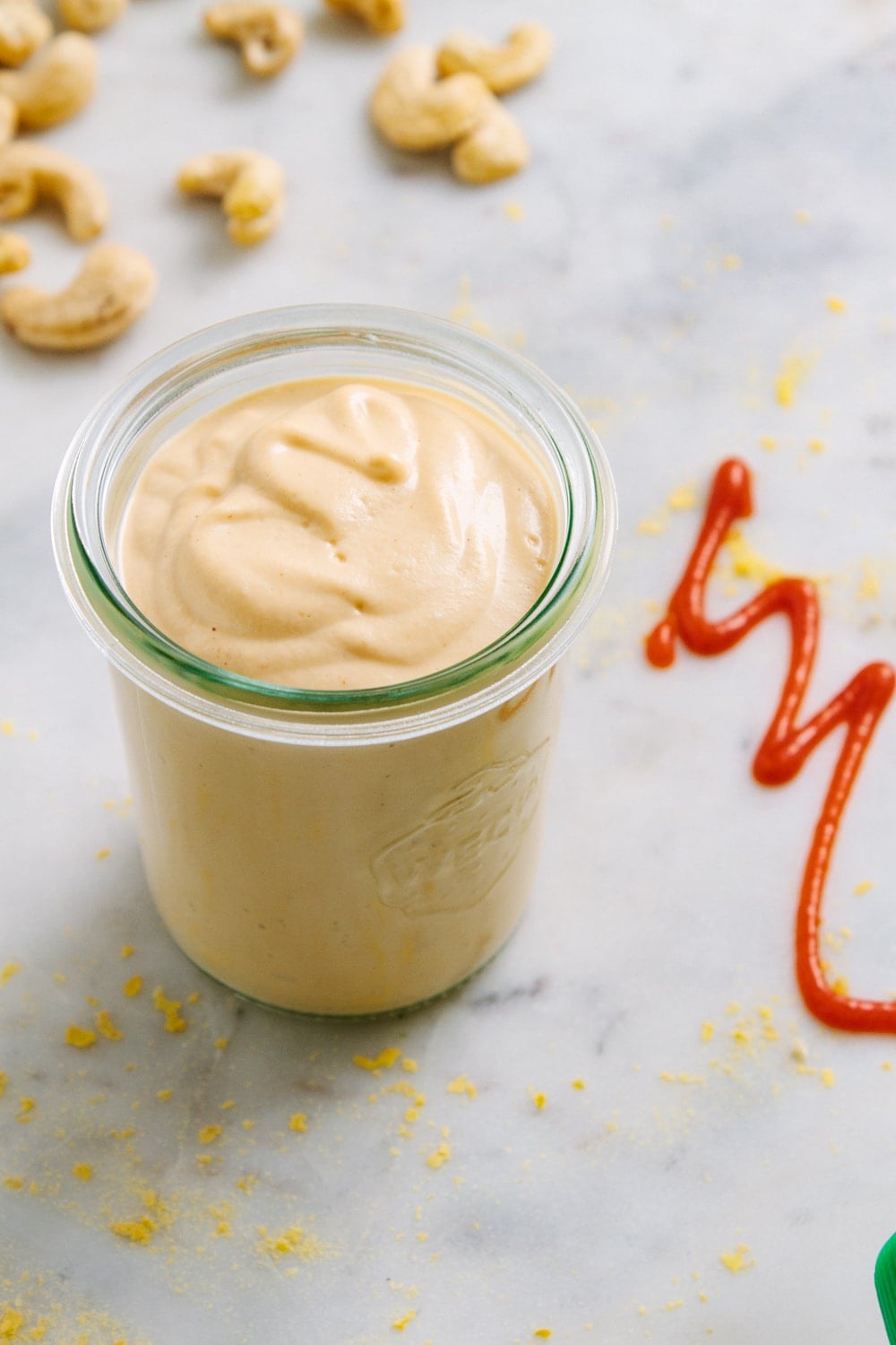 side angle view of sriracha cashew cheese sauce in a small glass jar.
